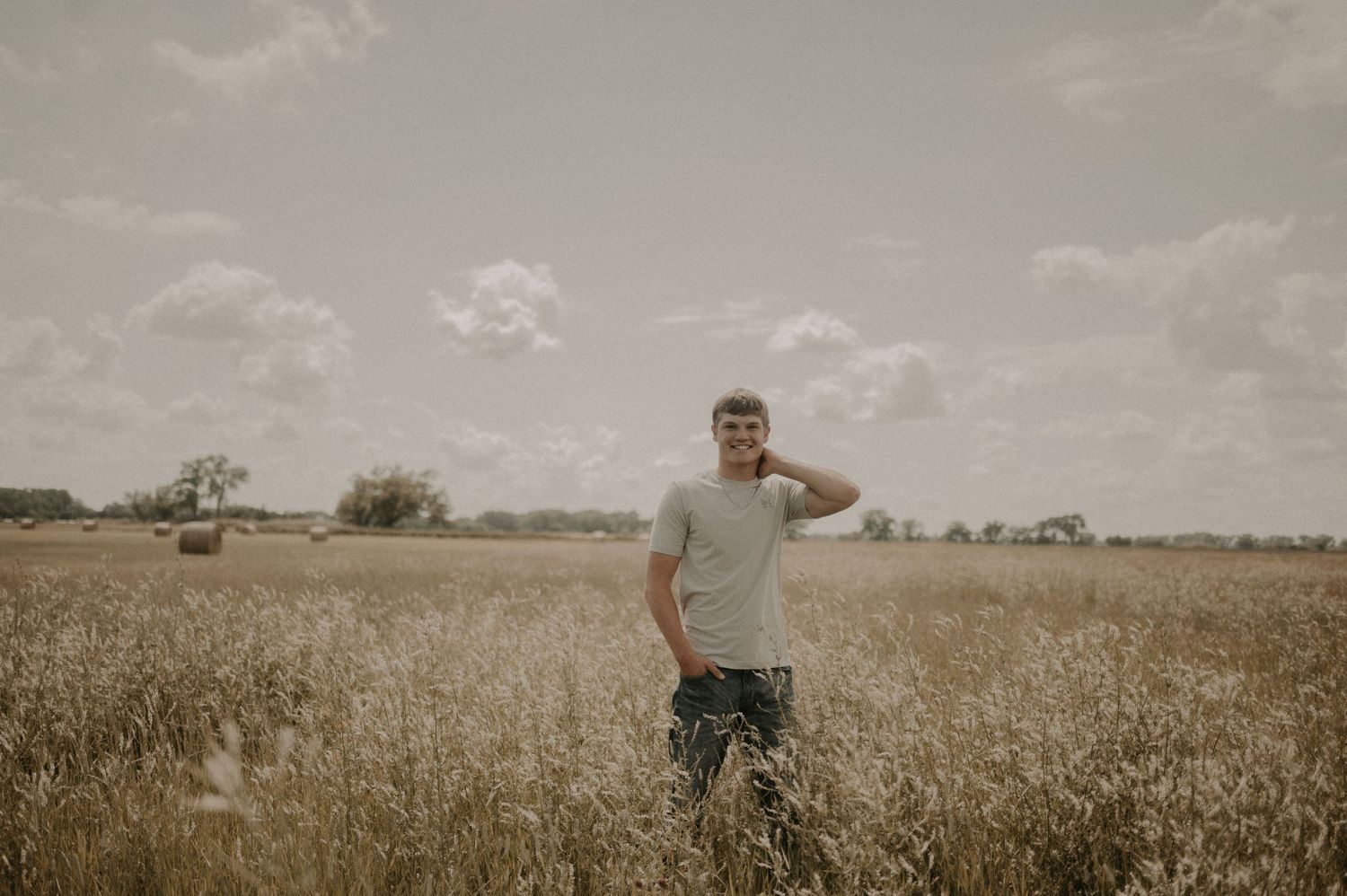 A panoramic view of a golden wheat field stretches to the horizon under a cloudy summer sky.
