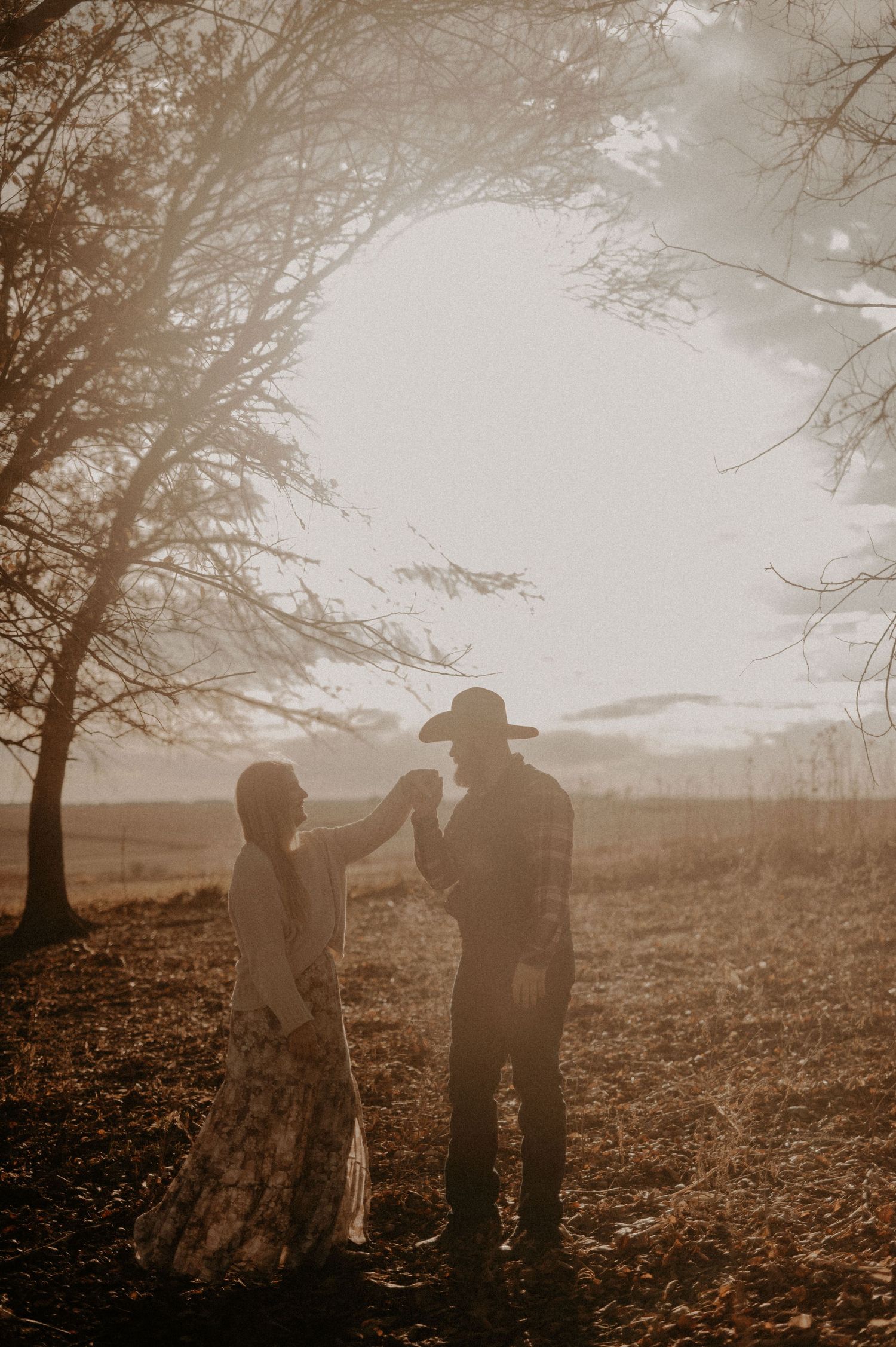 Two figures standing in fallen leaves beneath bare trees during golden hour.