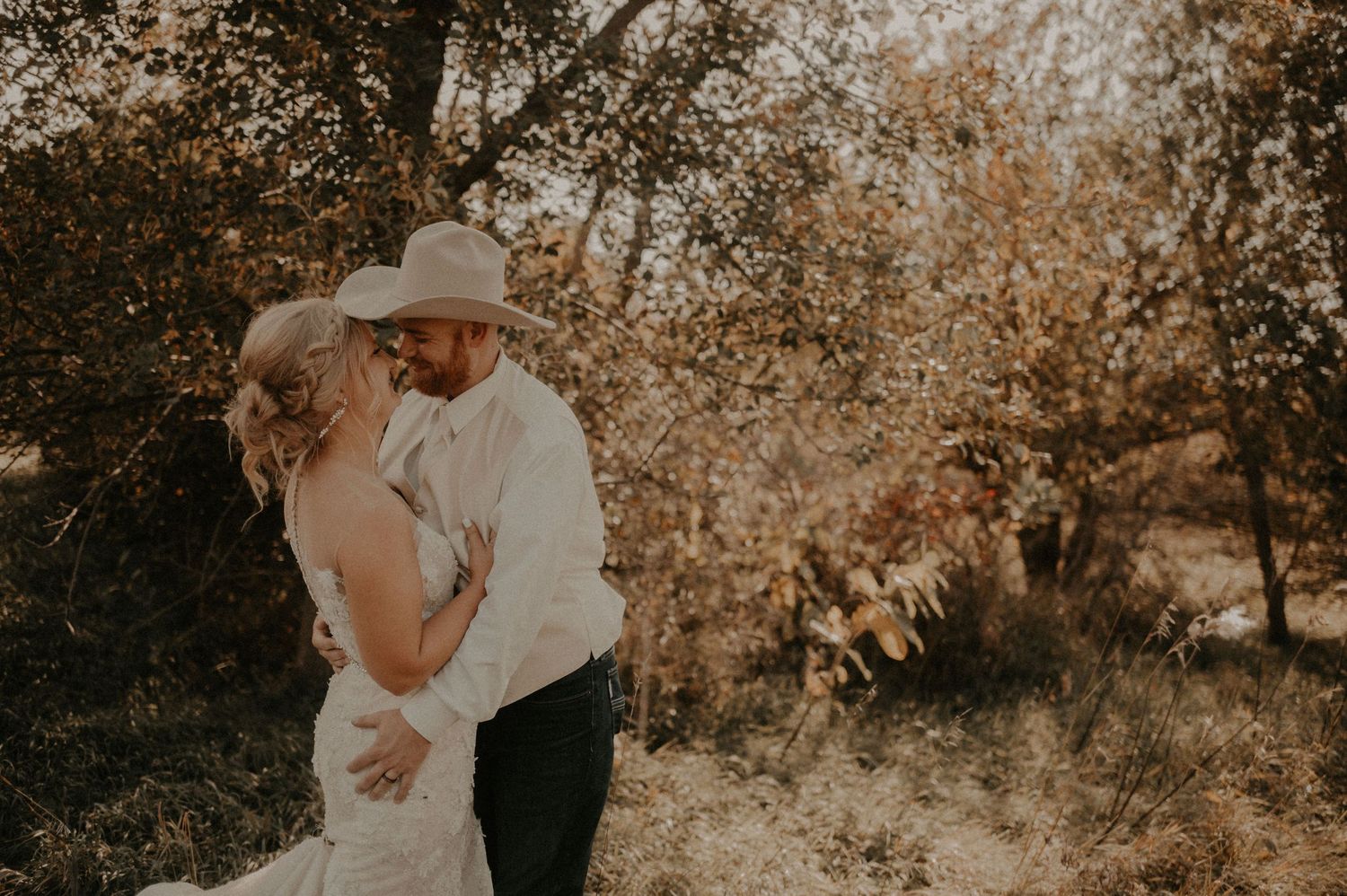 Romantic wedding couple embracing under golden sunlit trees.
