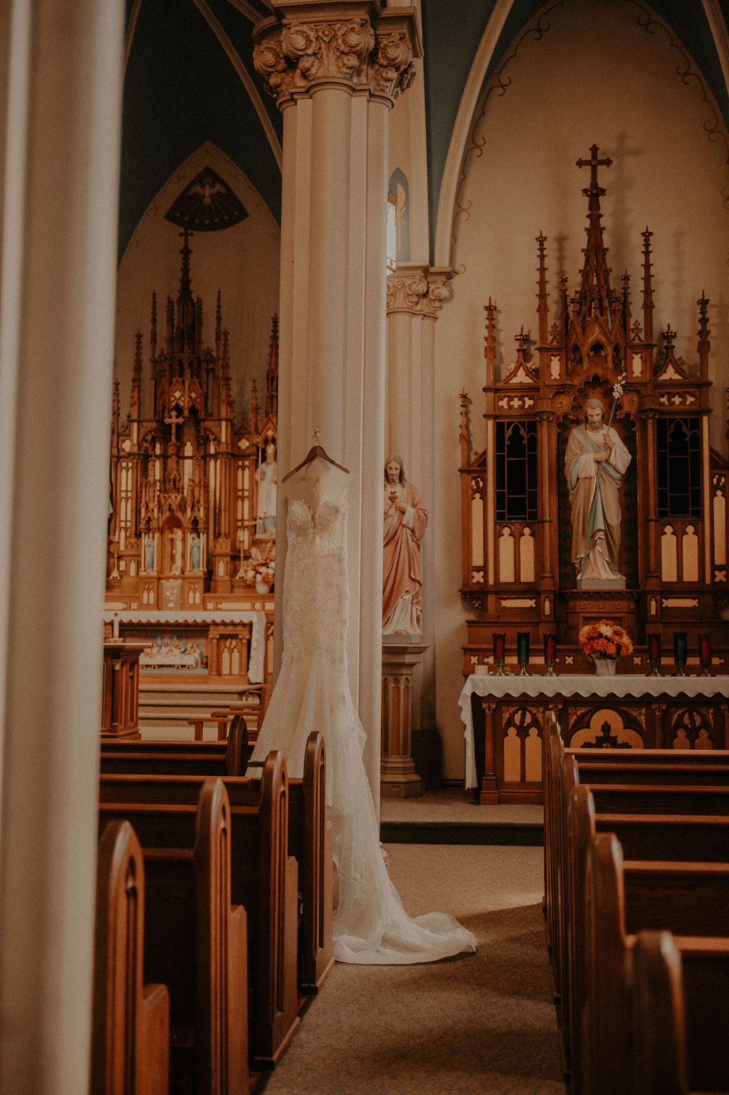 Church sanctuary with wooden pews, gothic architecture, and a white wedding dress displayed near the altar.