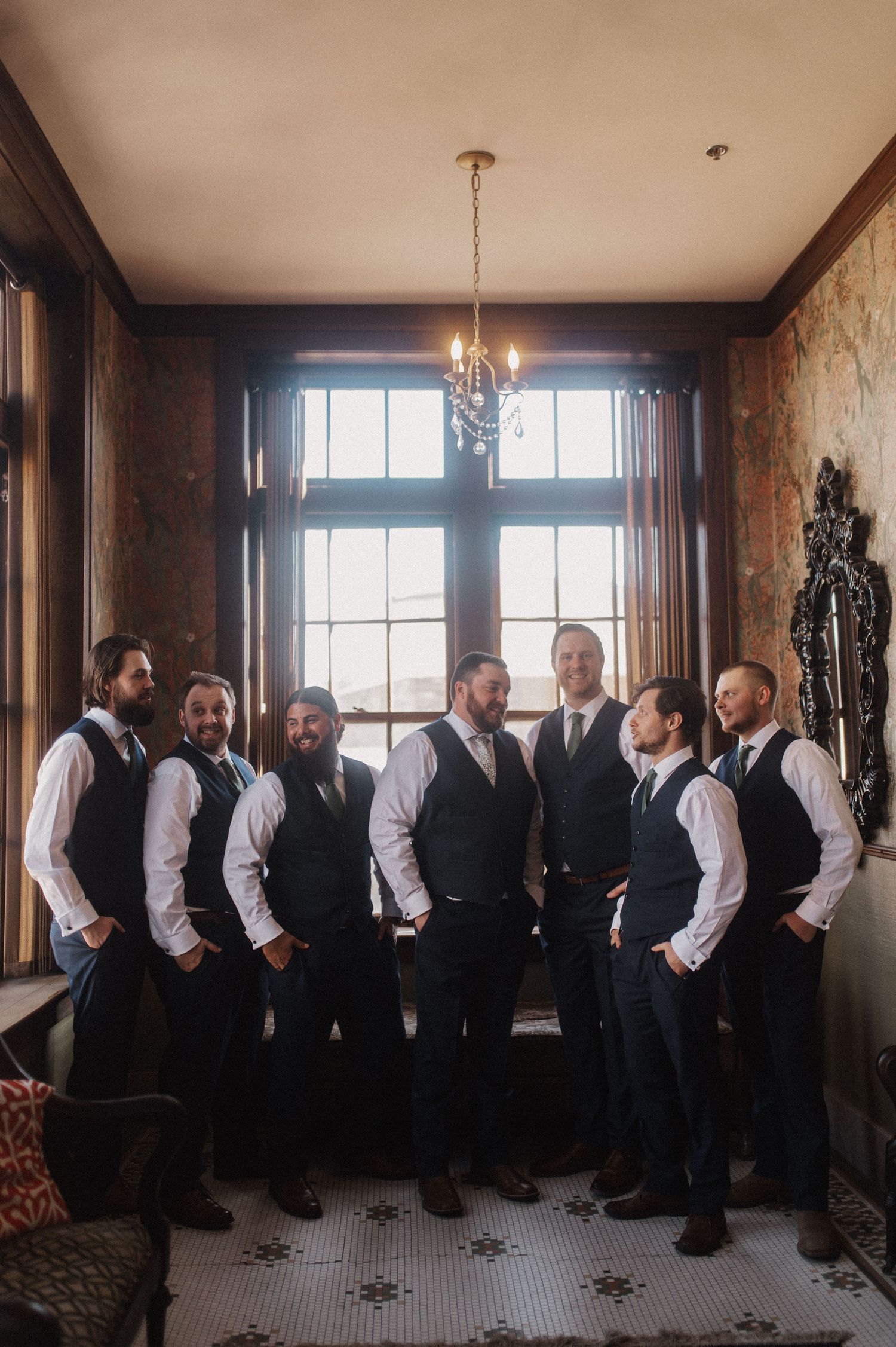 Groomsmen in black vests and white shirts line up in an elegant indoor venue.