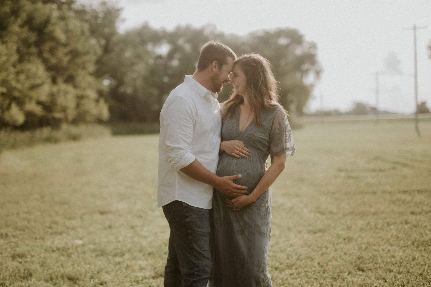 Couple embracing in a serene outdoor field during golden hour.