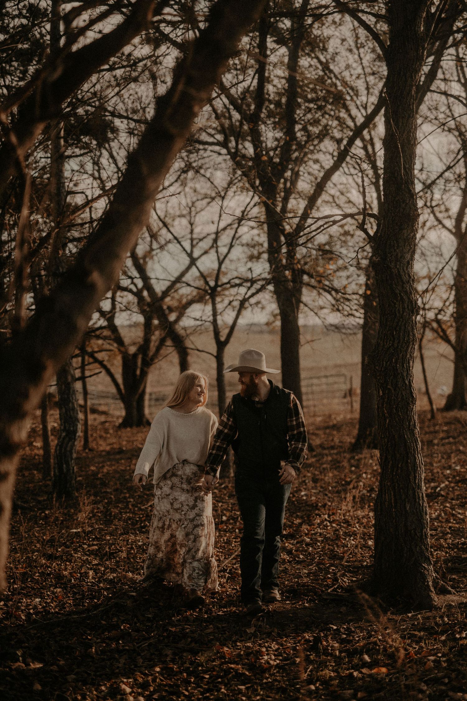 Two people walking among tall trees in a moody autumn forest setting.