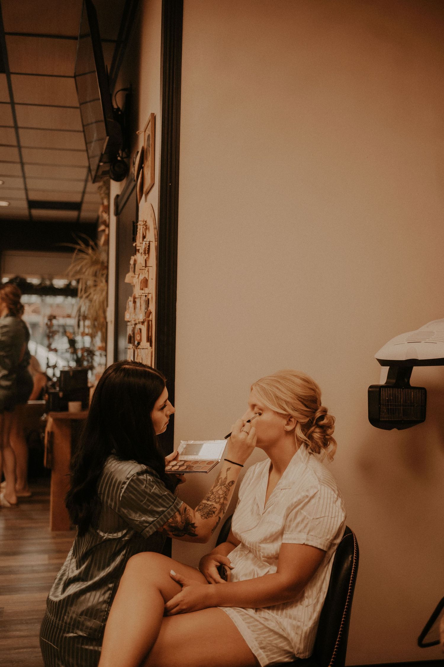 A makeup artist applies cosmetics to a client in a warm-toned salon setting.