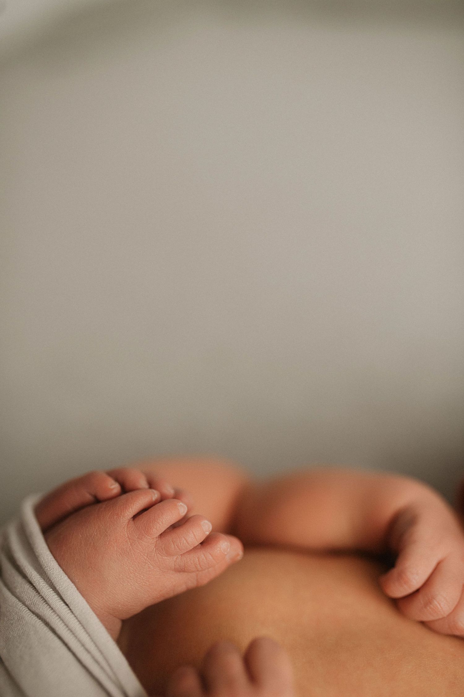 Close-up of tiny newborn feet and hands with white fabric wrapping.