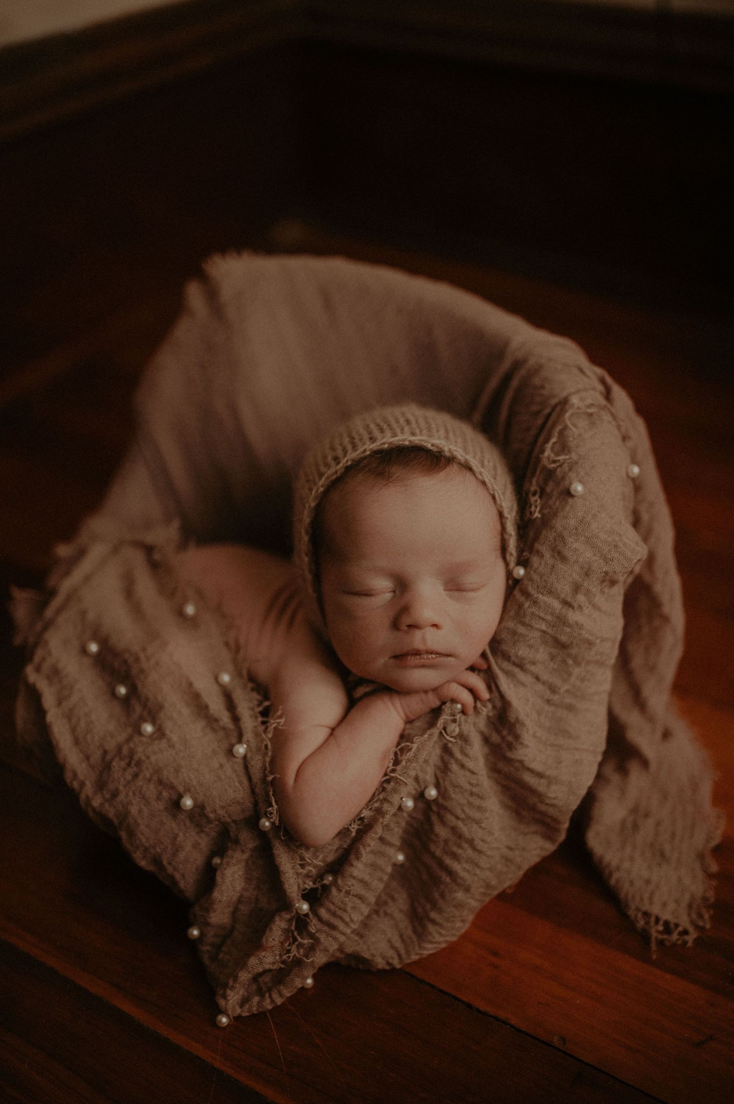 Moody newborn portrait on wooden surface with textured wrap and warm lighting.