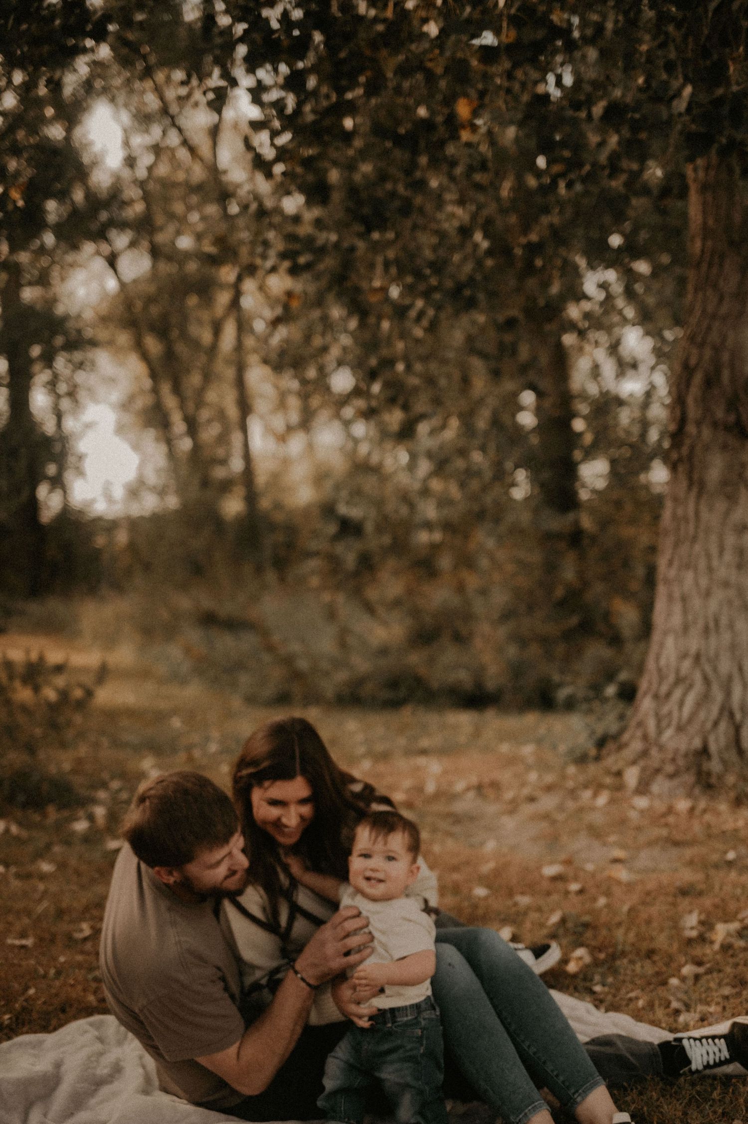 Family laughing together while relaxing on fallen leaves in an autumn forest.