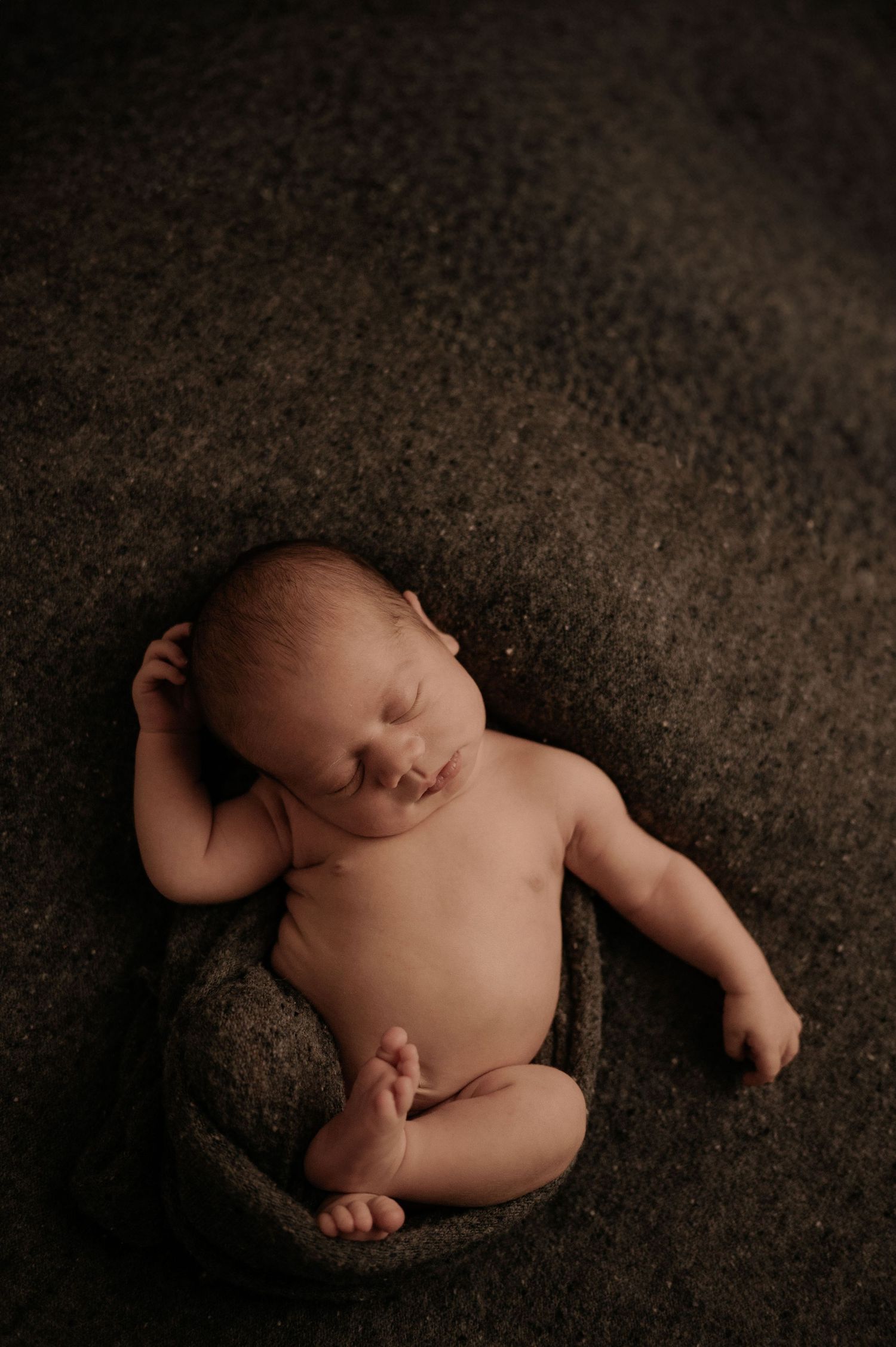 Artistic newborn photography on dark textured background in minimalist style.