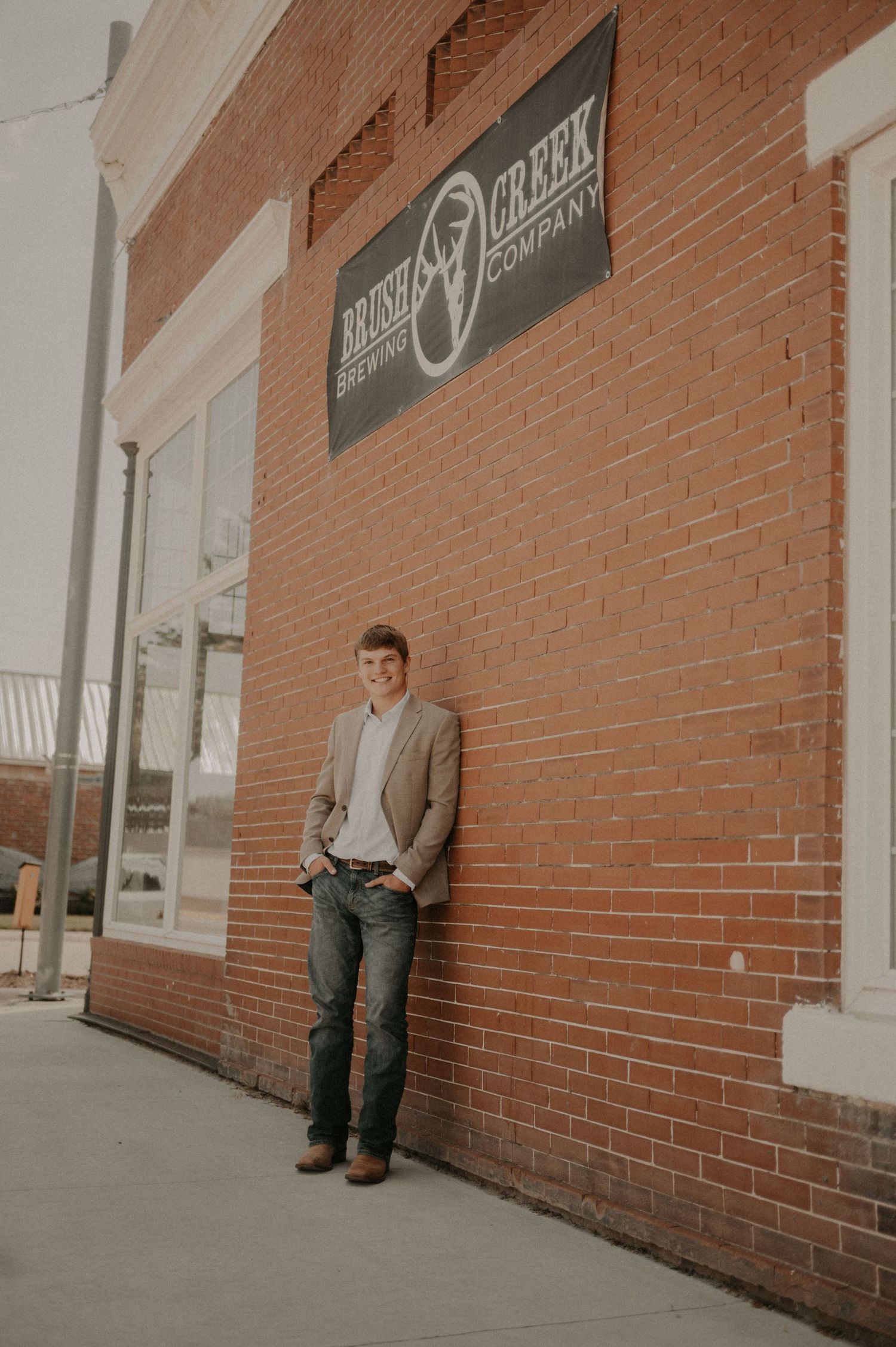 A person in casual attire stands against a brick wall outside a building with signage.