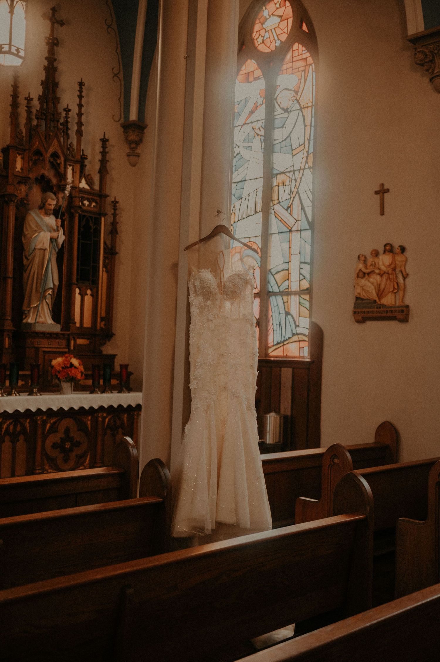 Interior of a church with ornate gothic details, stained glass windows, and a white dress on display.