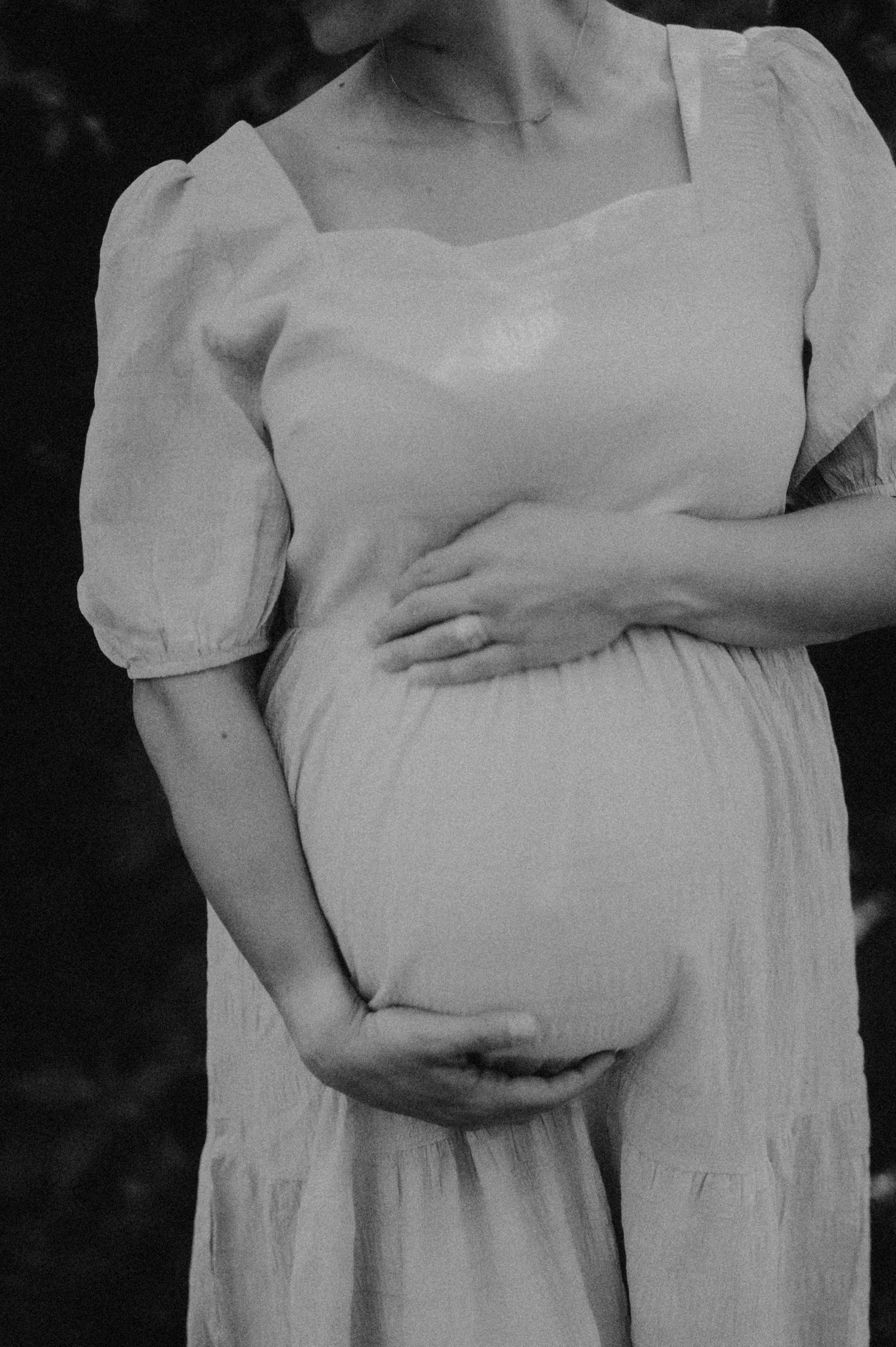 A series of black and white maternity photos showing a pregnant woman's belly in a white dress with hands cradling the bump.