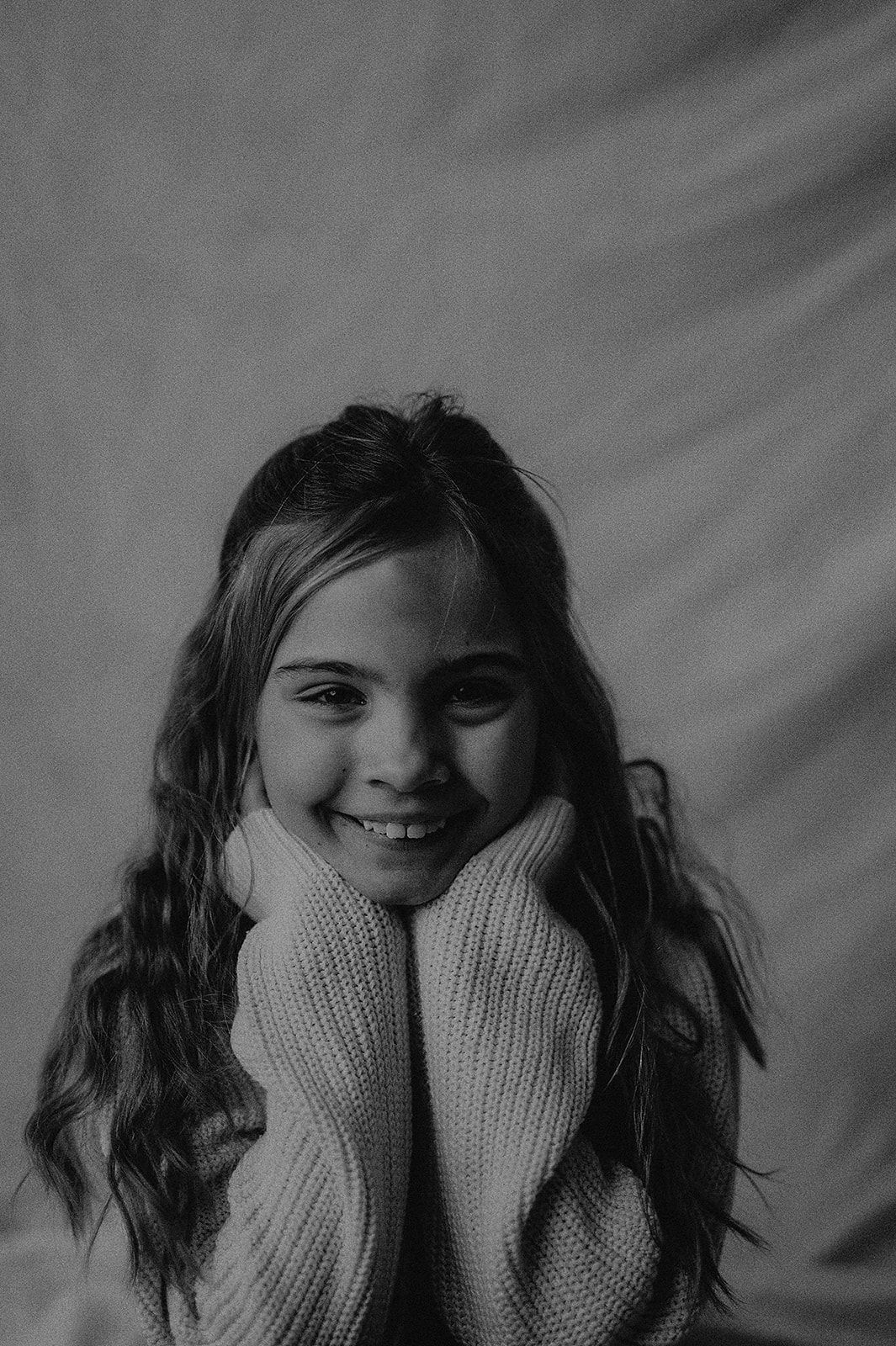 Black and white portrait of a child in a knit sweater with long dark hair and a joyful expression.