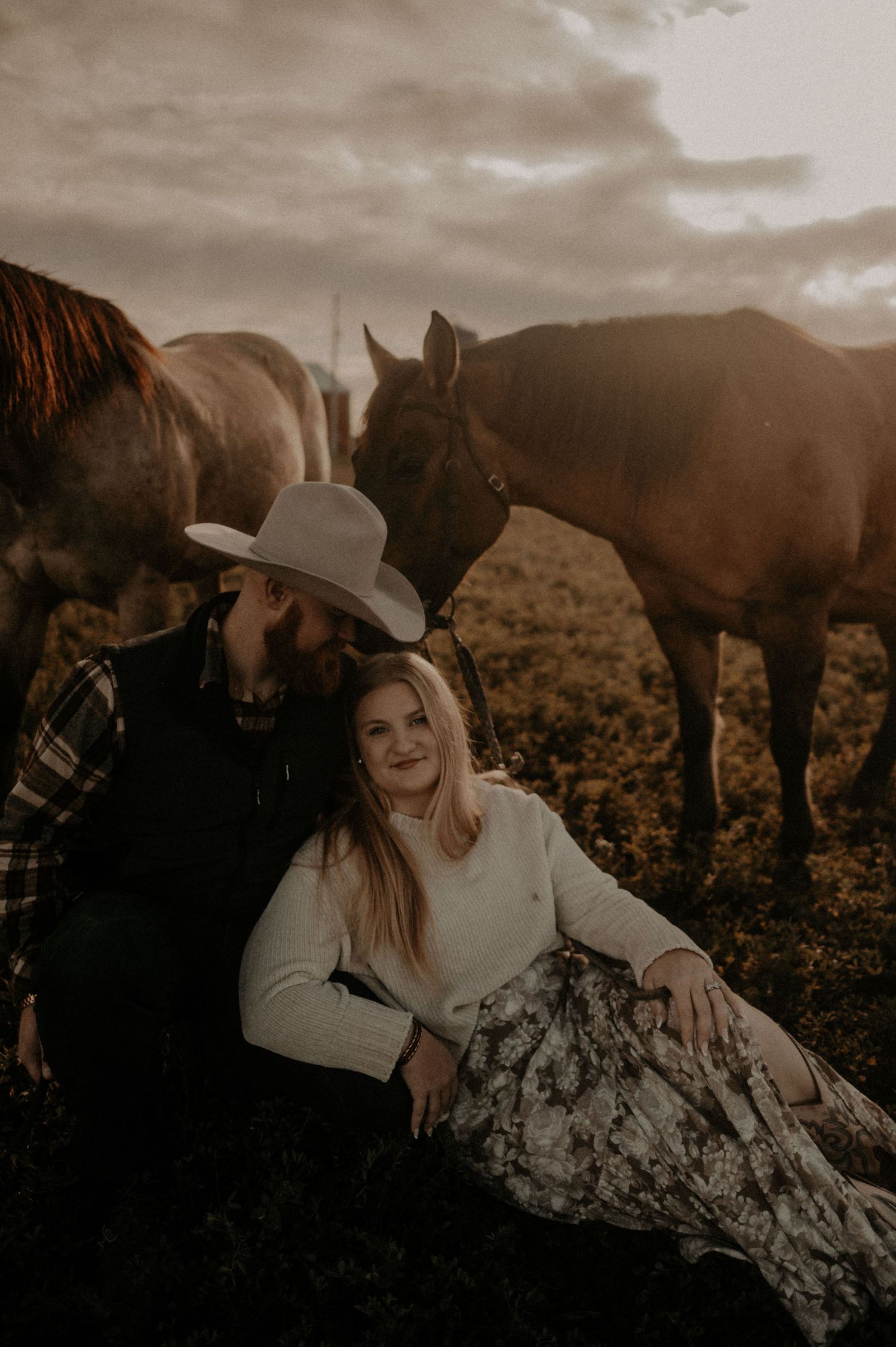 Intimate outdoor portrait session with horses grazing in a rustic field at sunset.