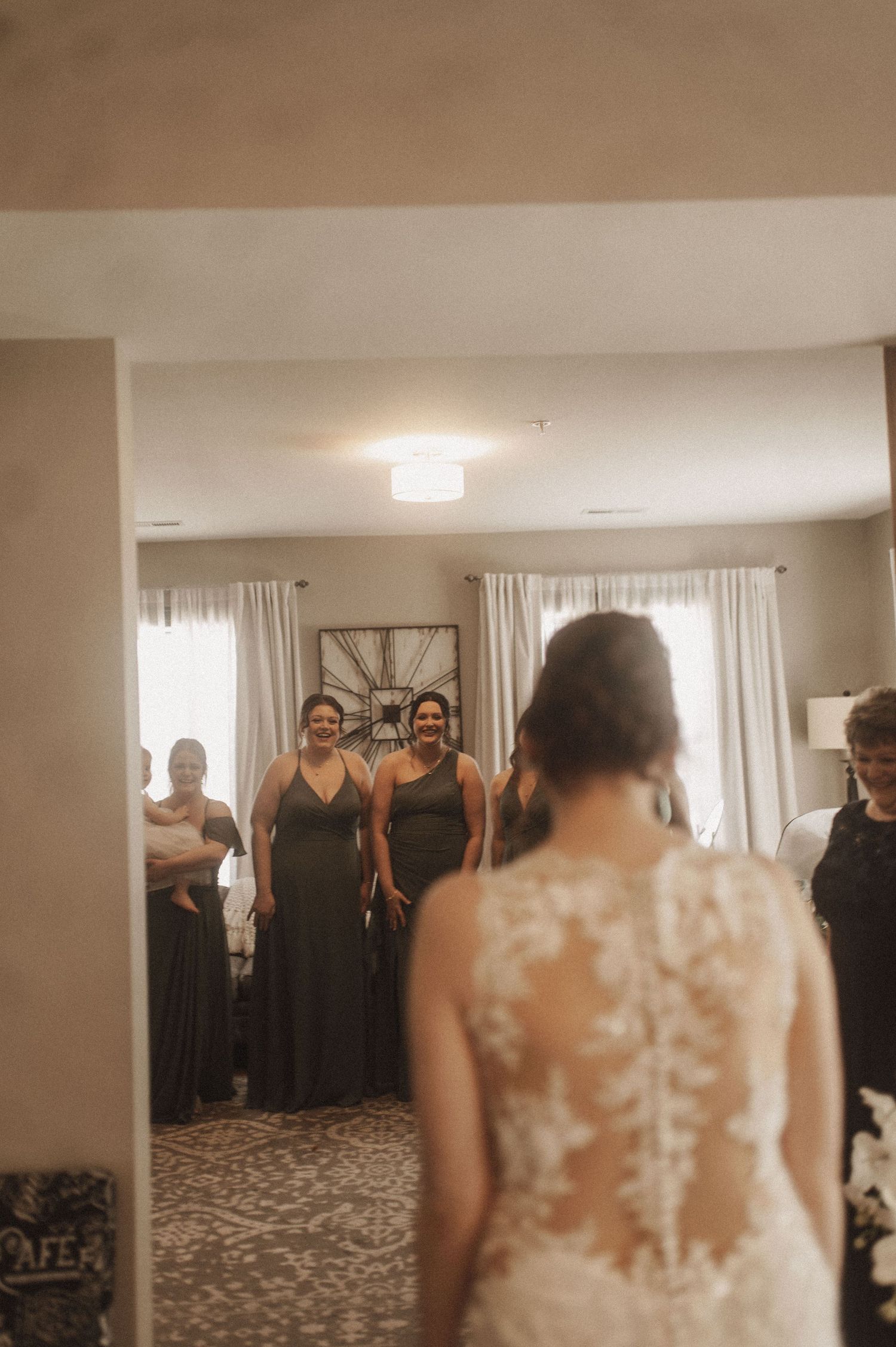 A wedding party gathered in a bright room with white curtains and decorative floral arrangements.