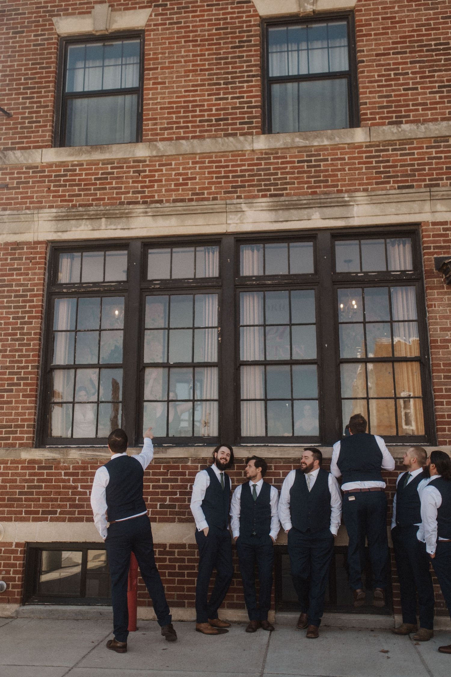 Students in formal attire line up outside a brick building with large windows.