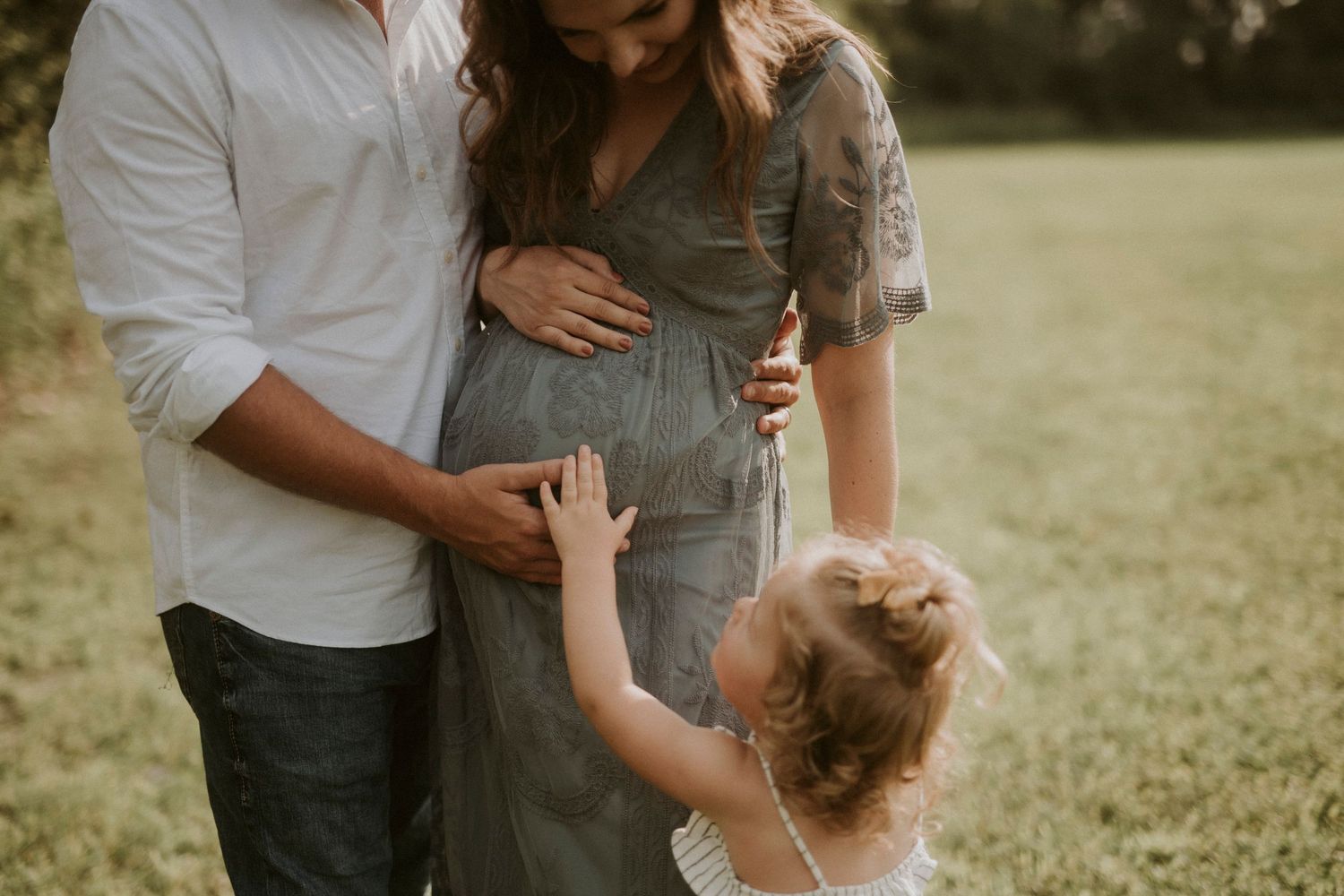 A family shares tender moments together in a sun-drenched field during a casual outdoor photo session.