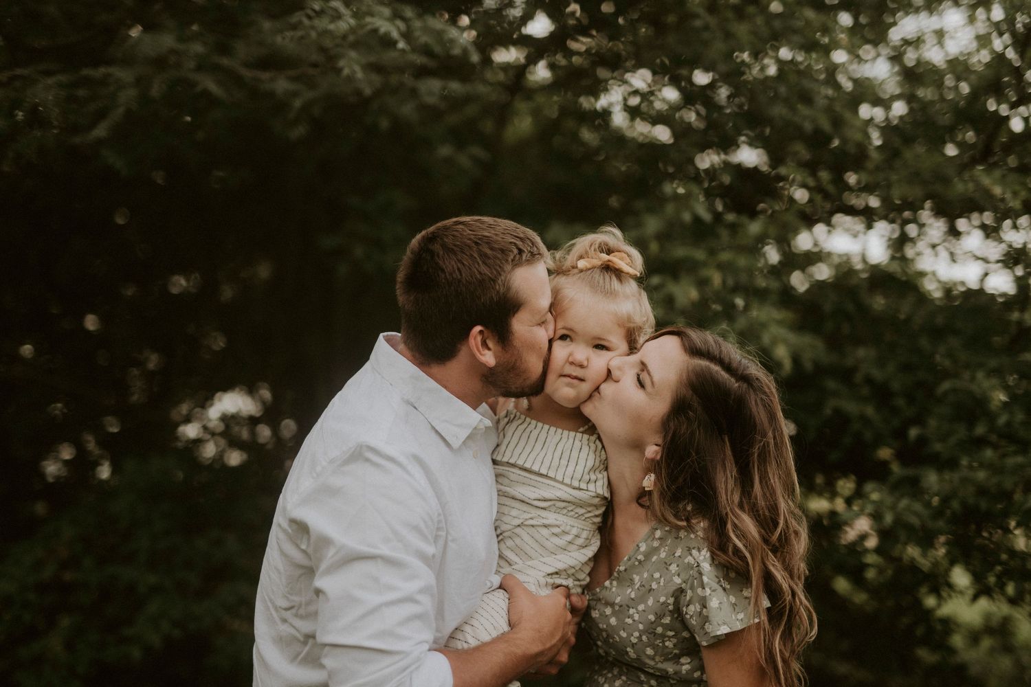 A family shares tender moments together in a series of outdoor portraits against a natural green backdrop.