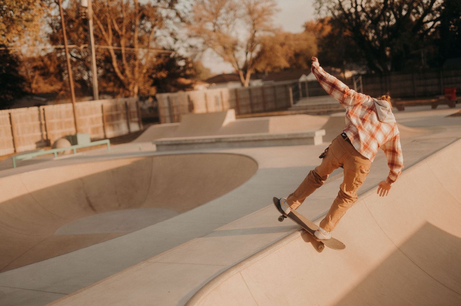Skateboarder performs tricks at a skate park during sunset with warm lighting.