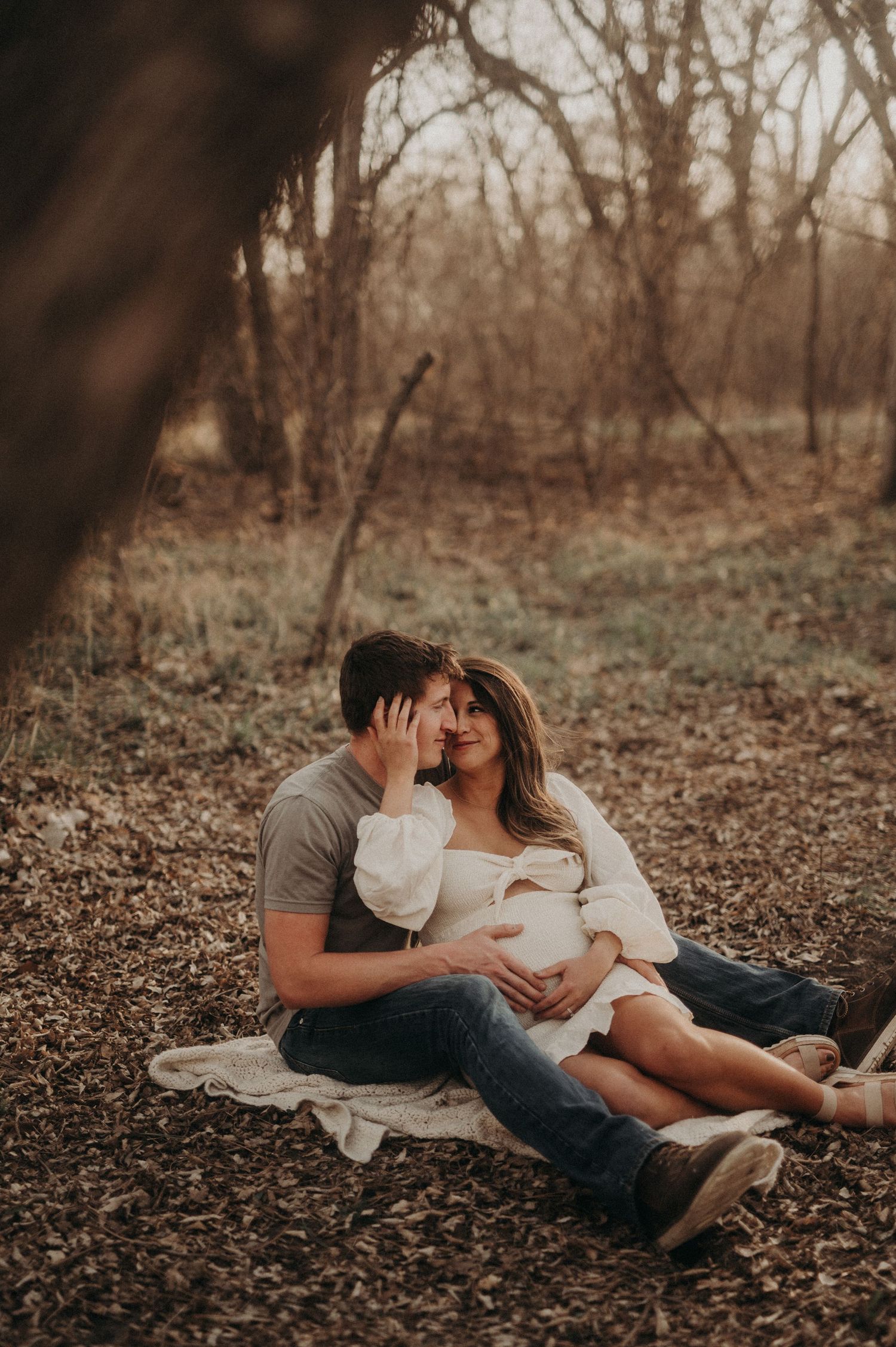 Intimate maternity photos of couple laying on fallen leaves in the woods.
