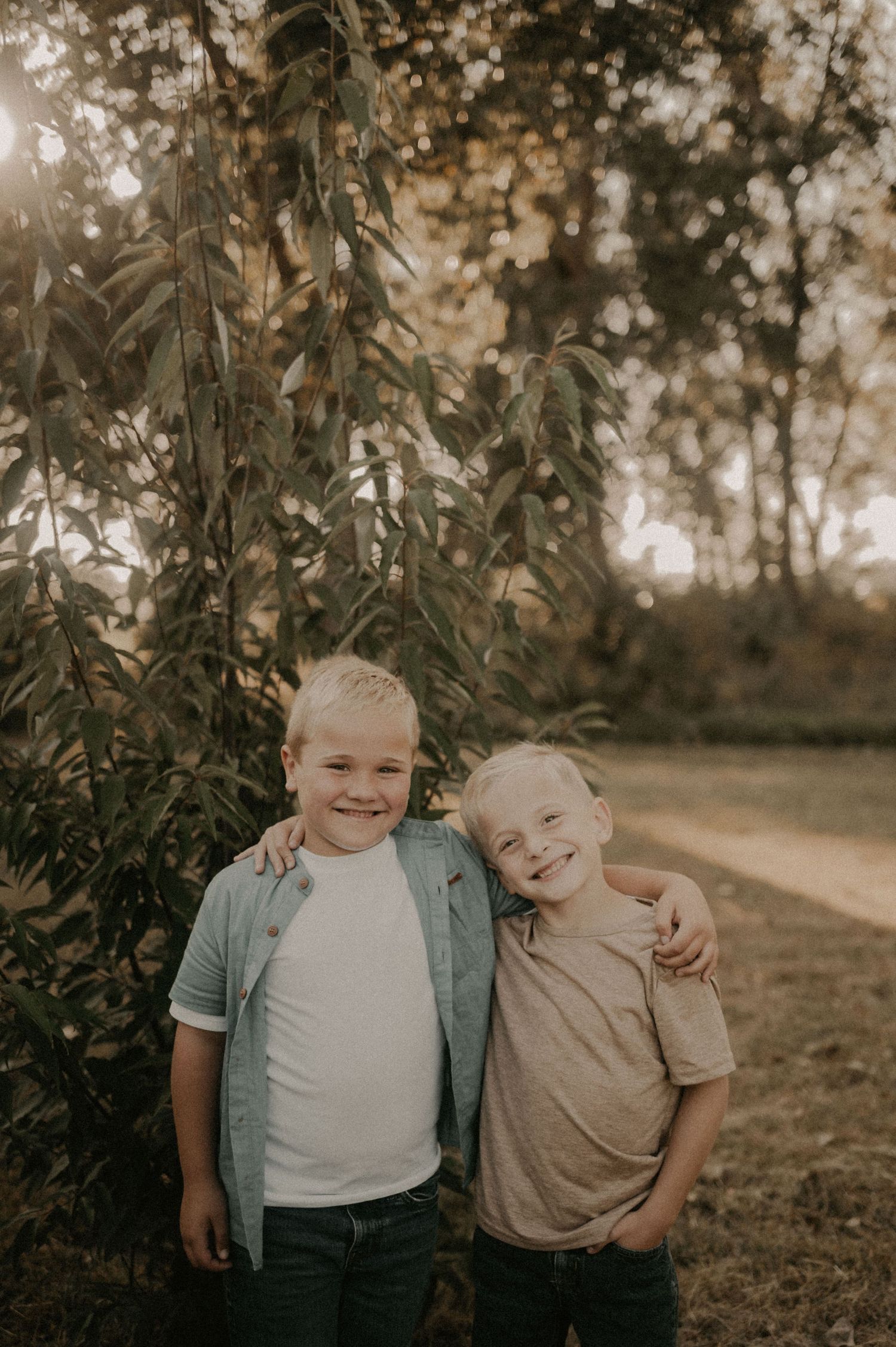 Two siblings share a playful moment outdoors against a natural backdrop.