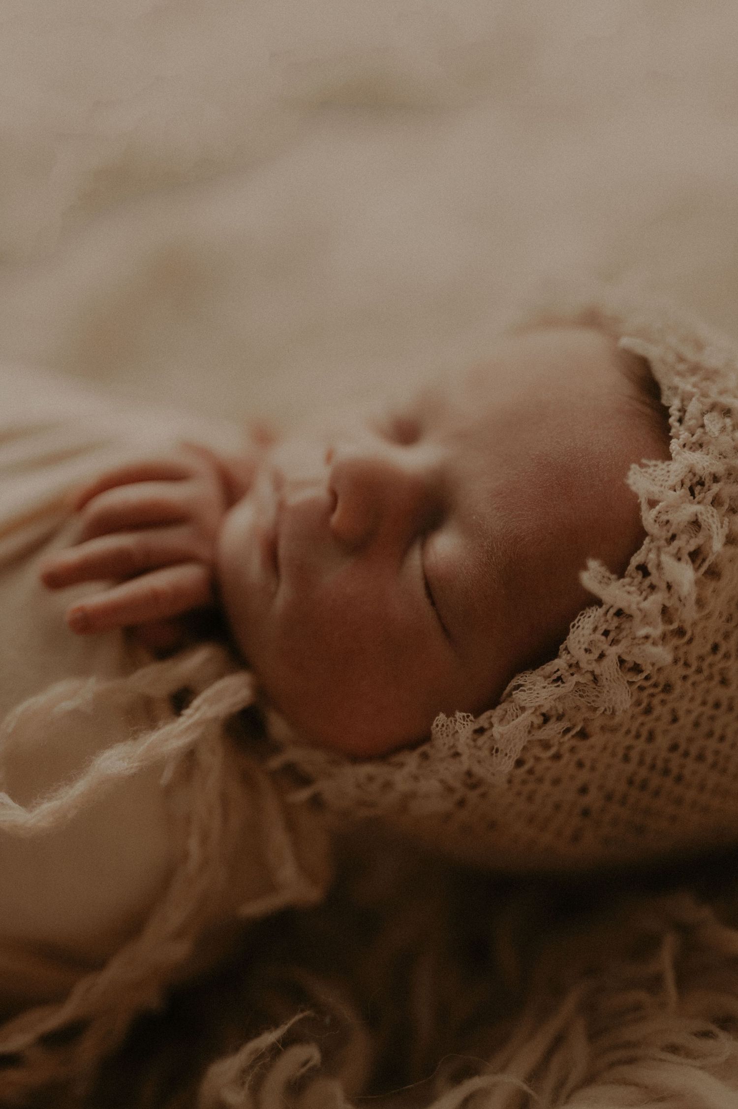 Sepia-toned close-up of sleeping baby with vintage lace details.