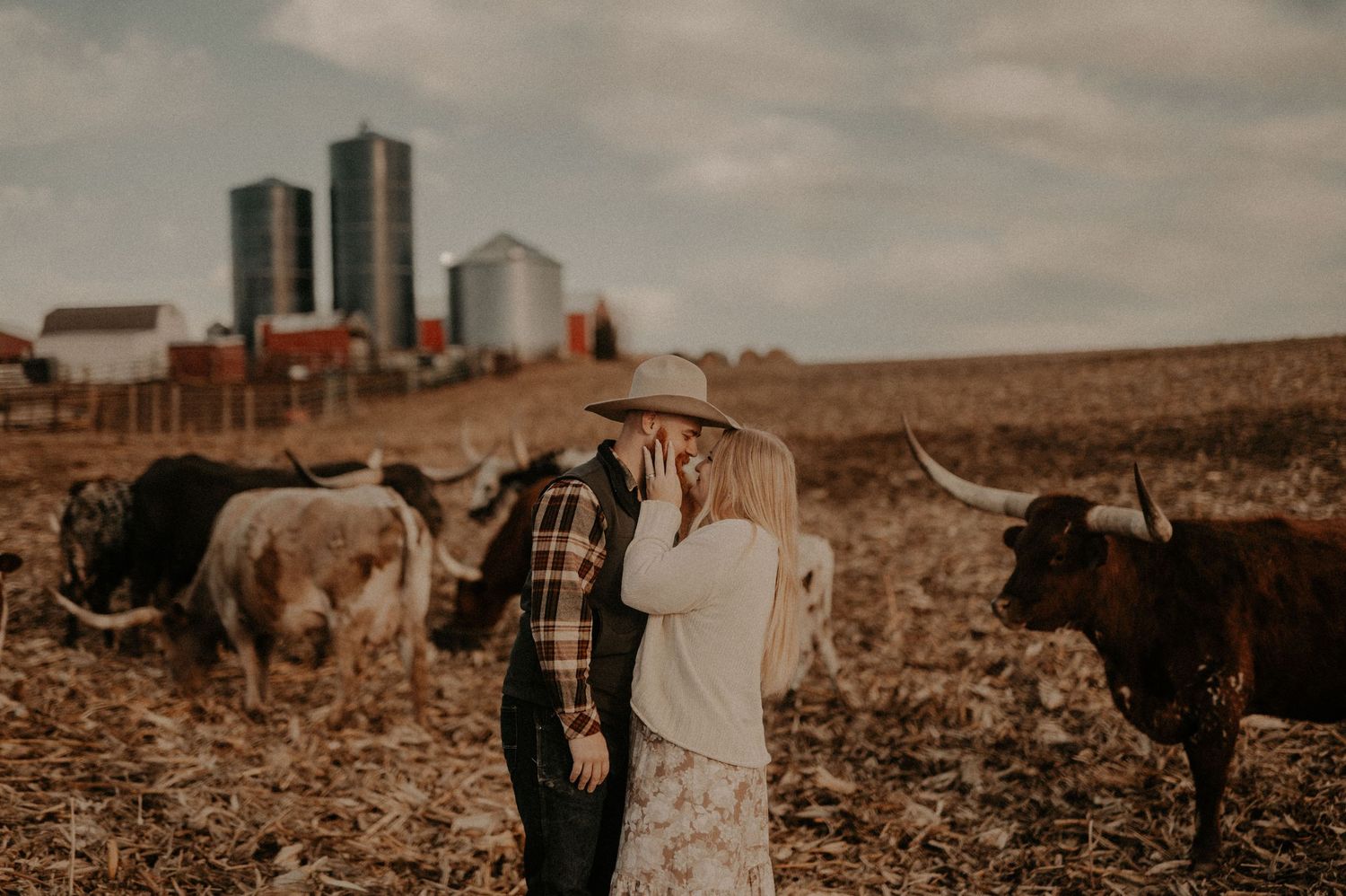 A couple stands together in a rustic farm field during sunset.