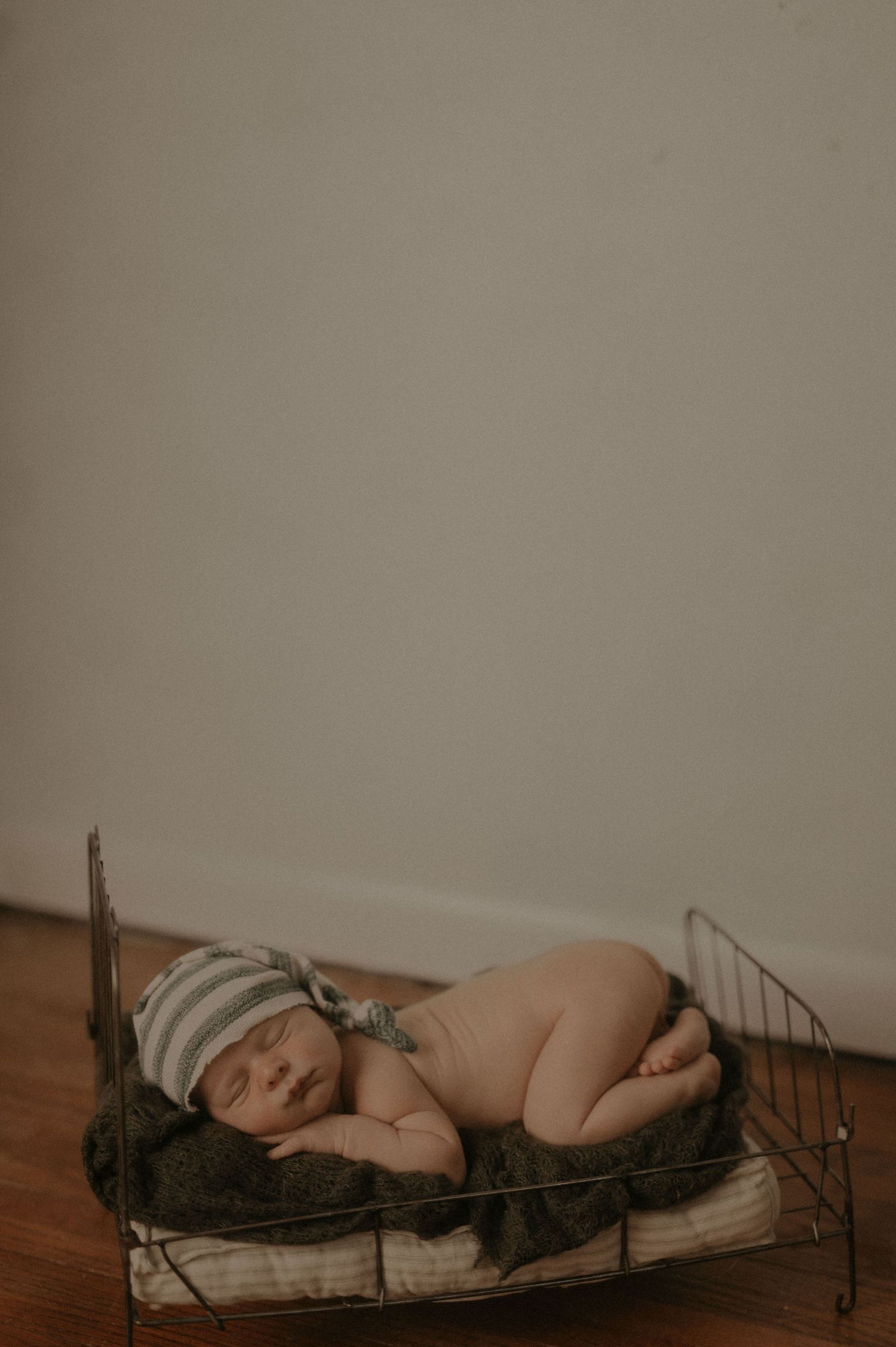 A sleeping baby lies peacefully on a vintage iron bed frame in a minimalist sepia-toned setting.