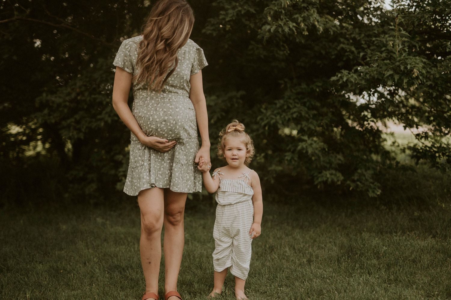 A loving family embraces while standing in a sunlit meadow surrounded by lush green trees.