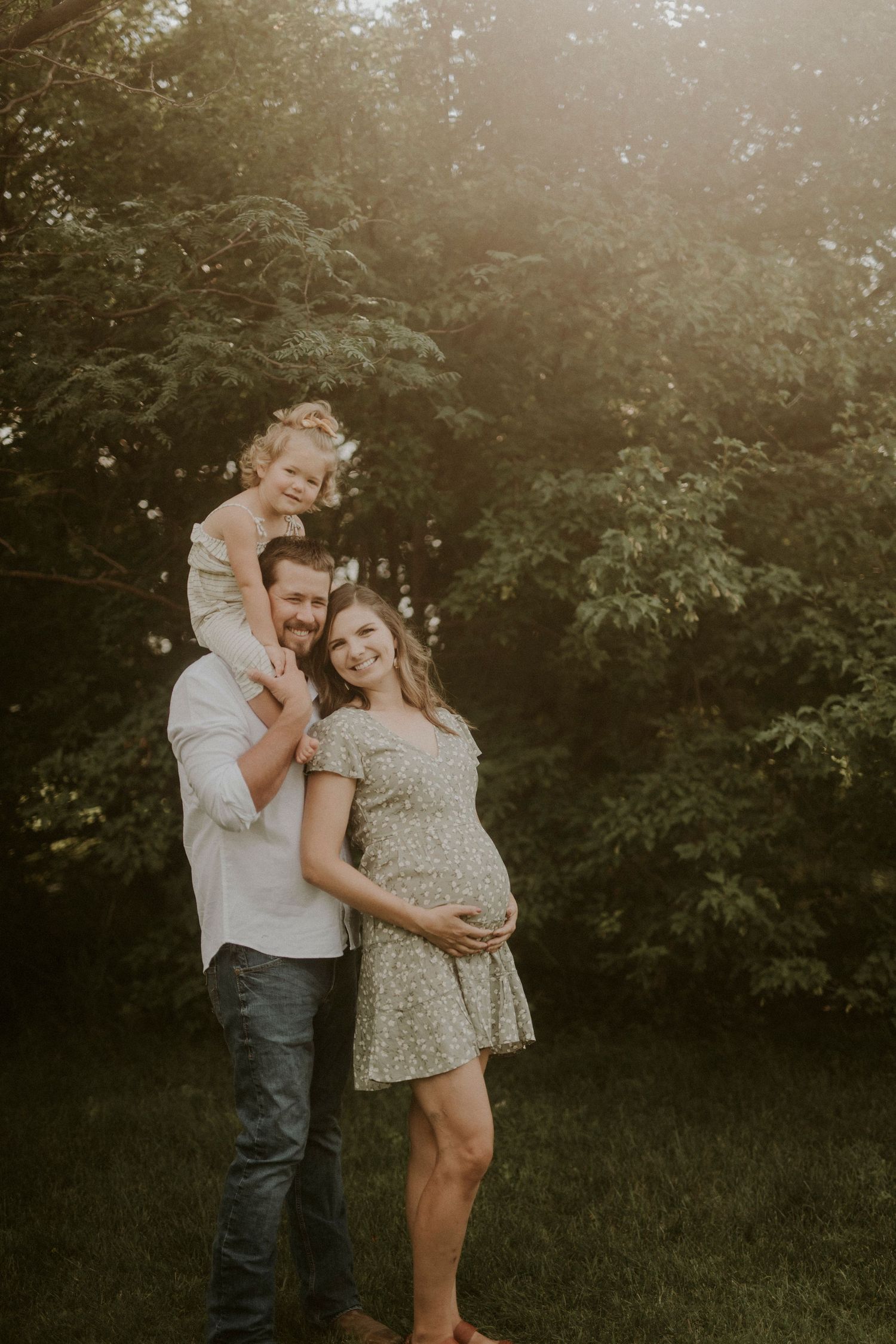 A couple shares a tender moment in a sunlit garden setting during a maternity photoshoot at golden hour.