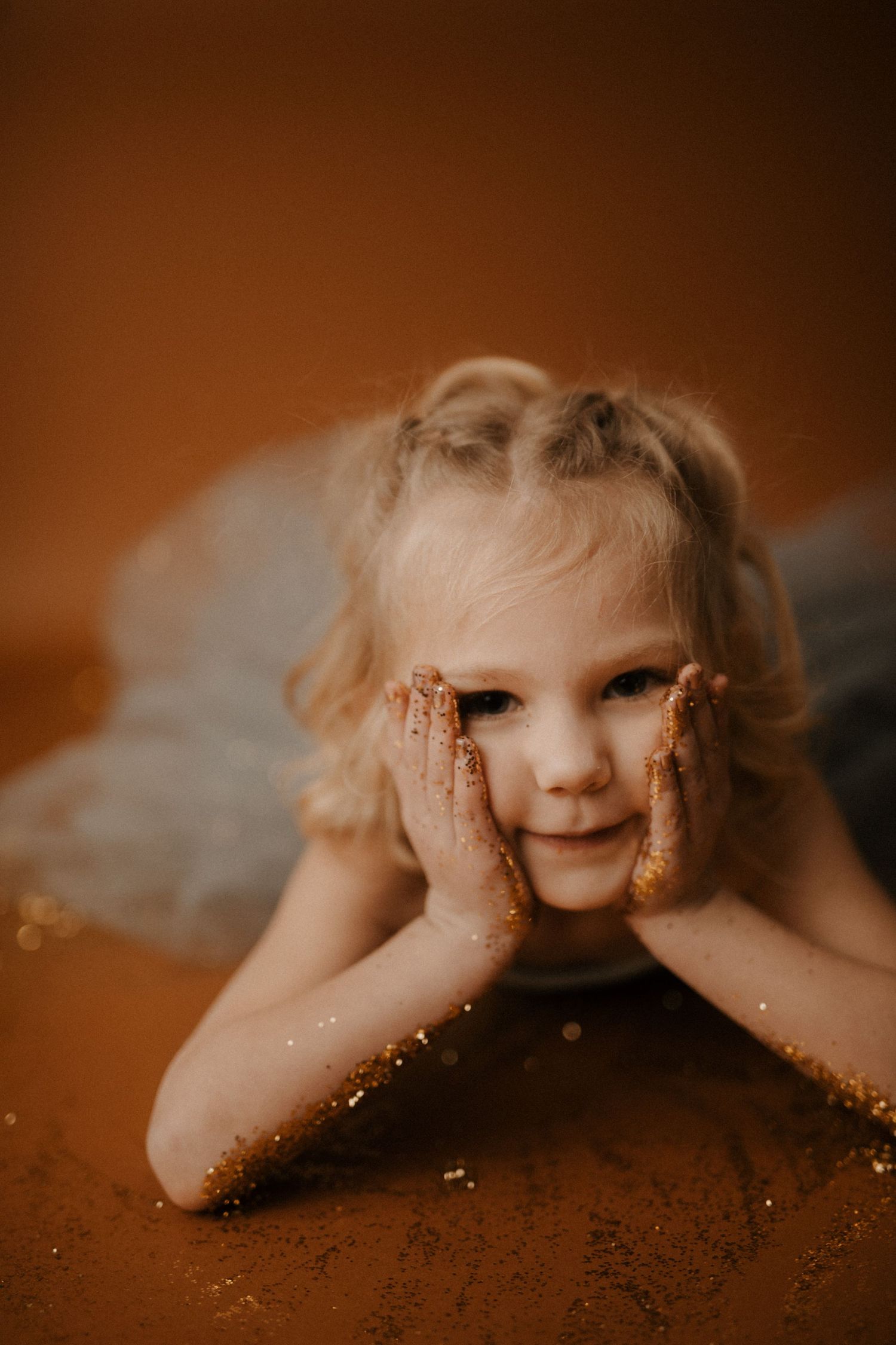 A creative portrait series showing a child peeking over a surface with glitter-covered hands in warm brown tones.