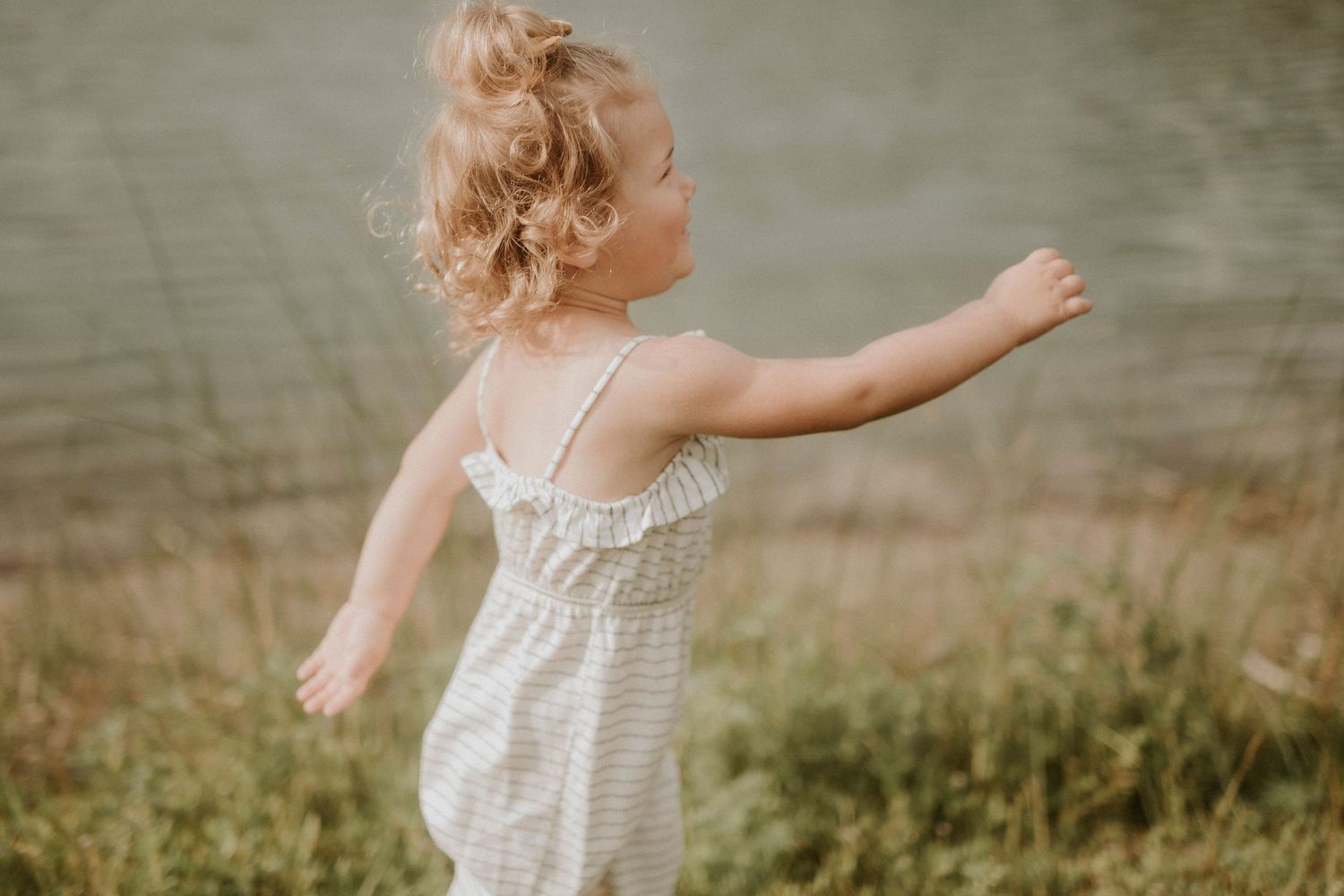 A child in a white summer dress runs playfully through a grassy field on a warm afternoon.