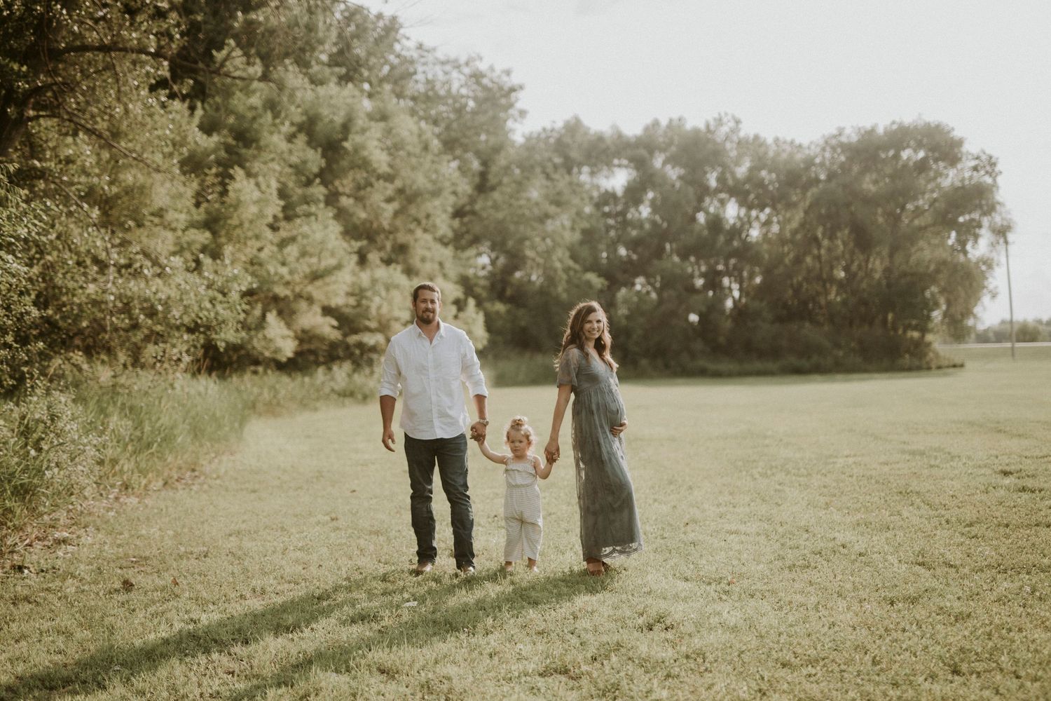 Family walking together through a sunny meadow holding hands on a warm summer afternoon.