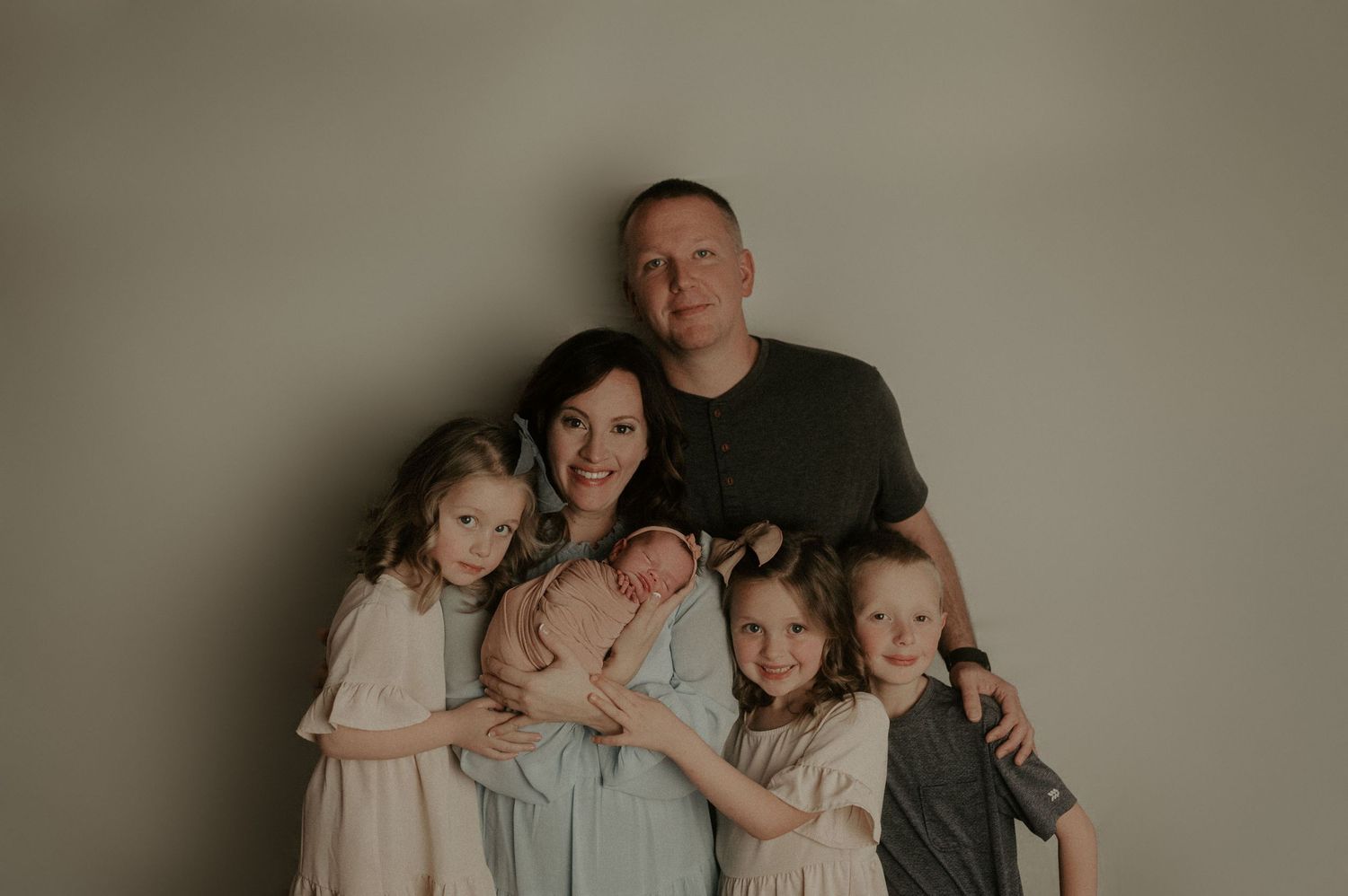 Family portrait showing parents and children together against neutral background.