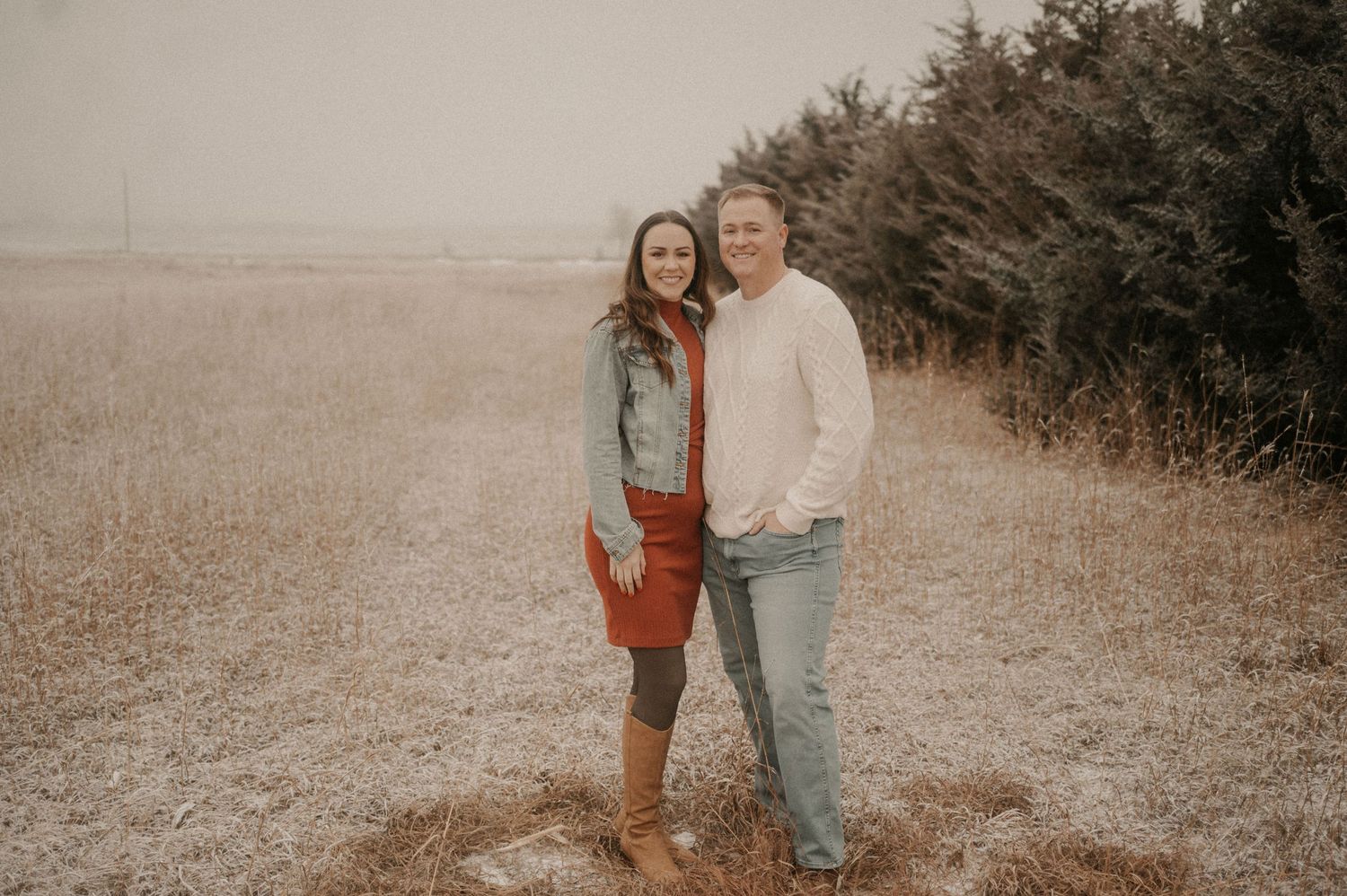 Two people in casual attire walking together through a rustic autumn field with muted brown tones.