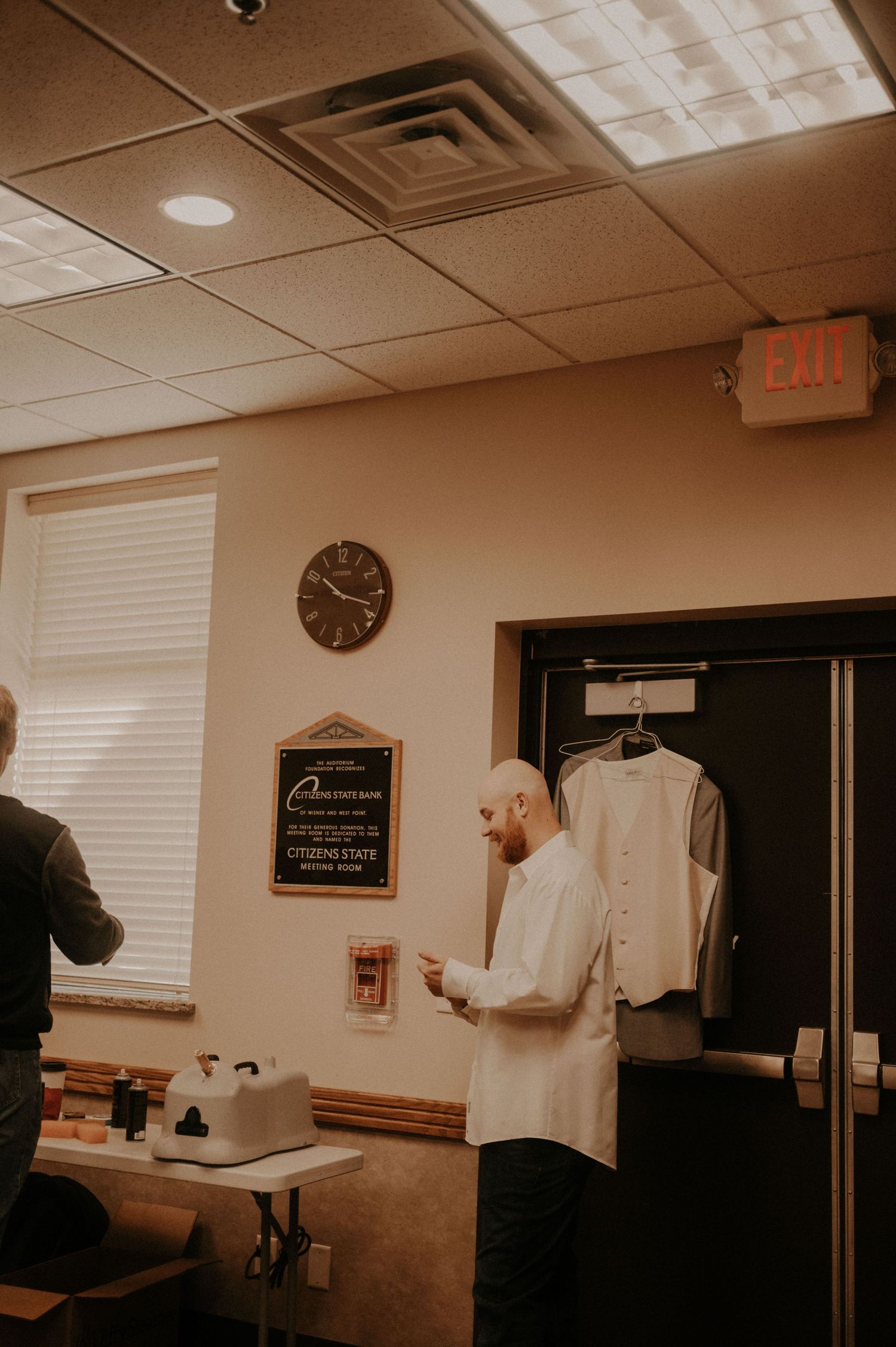 Interior room with exit sign, wall clock, and hanging garments visible.