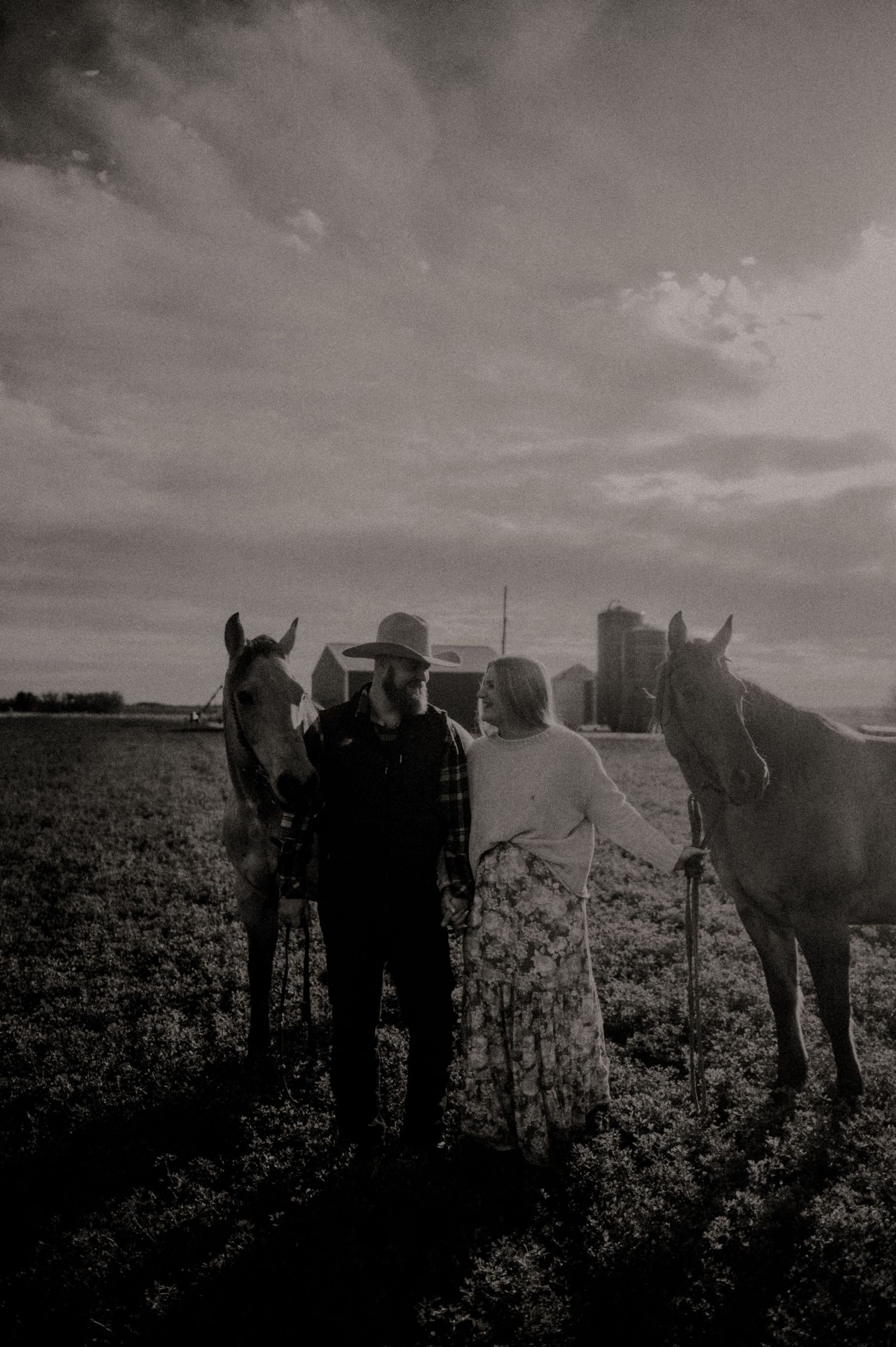 Silhouettes of people and horses stand together in a dramatic sunset landscape.
