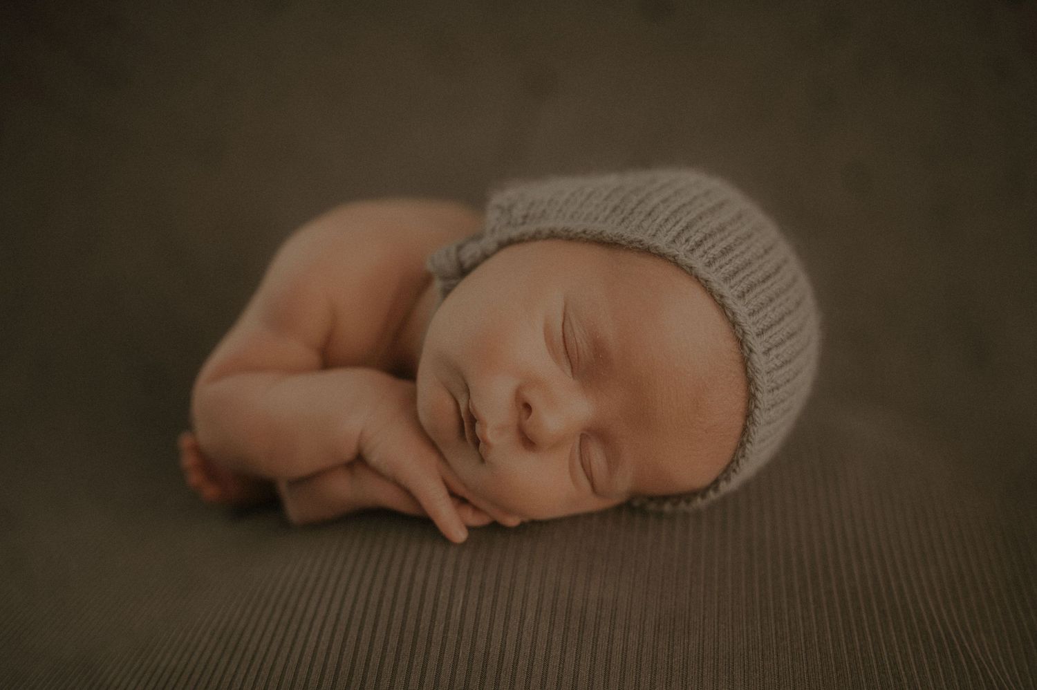 A peaceful newborn sleeps on a soft brown blanket in warm, moody lighting.