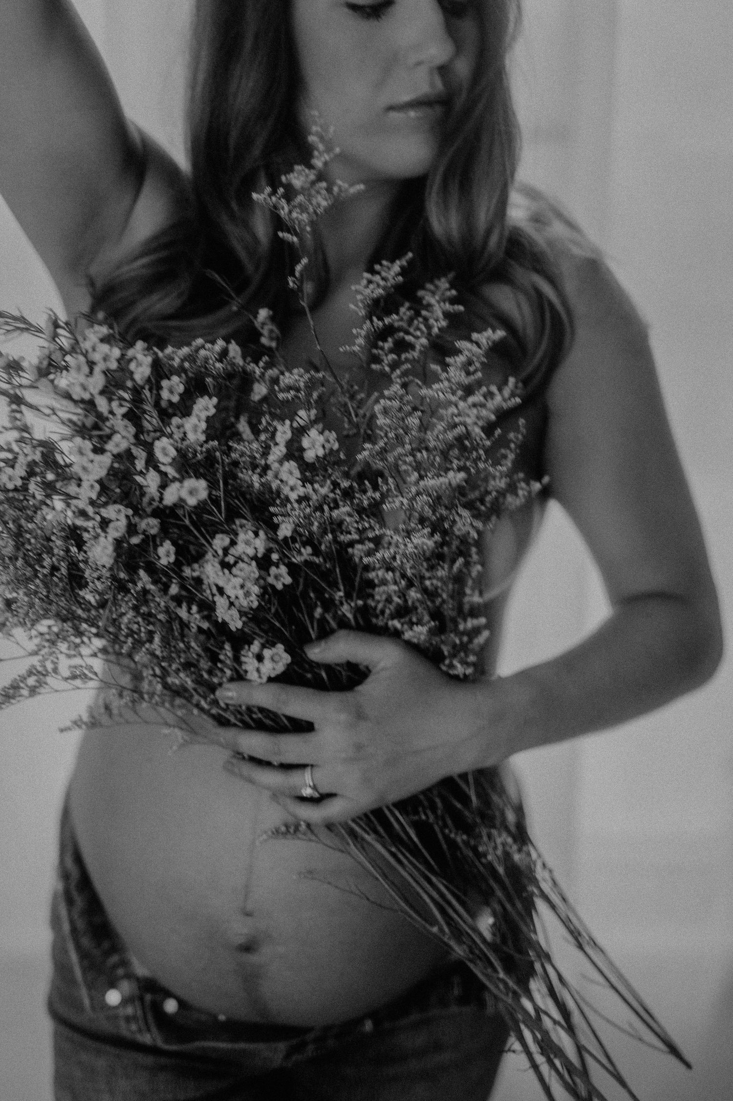 Artistic black and white photo of a woman holding dried flowers against a light background.
