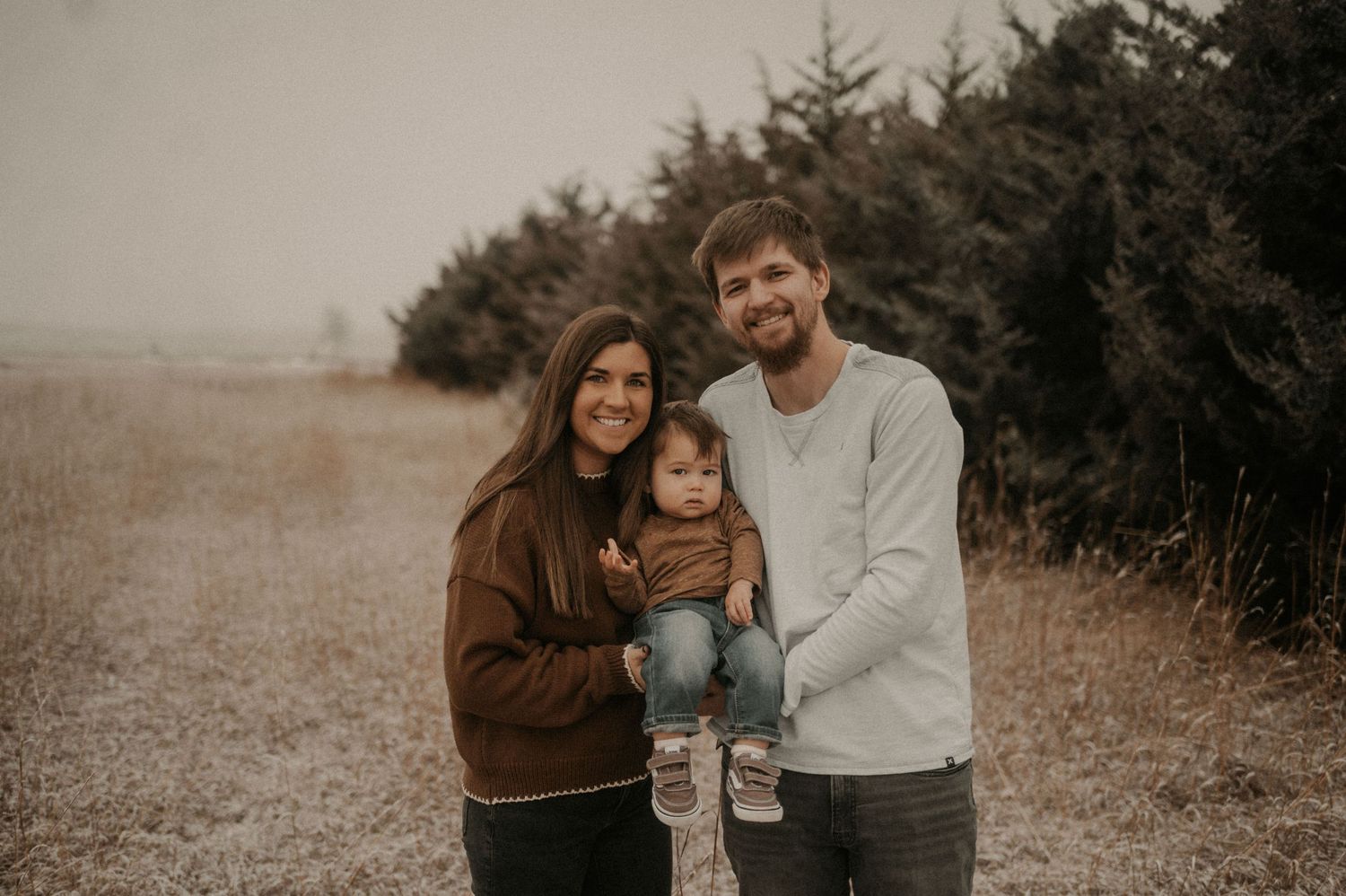 A couple shares intimate moments in a field during a romantic outdoor photoshoot with a moody, desaturated aesthetic.