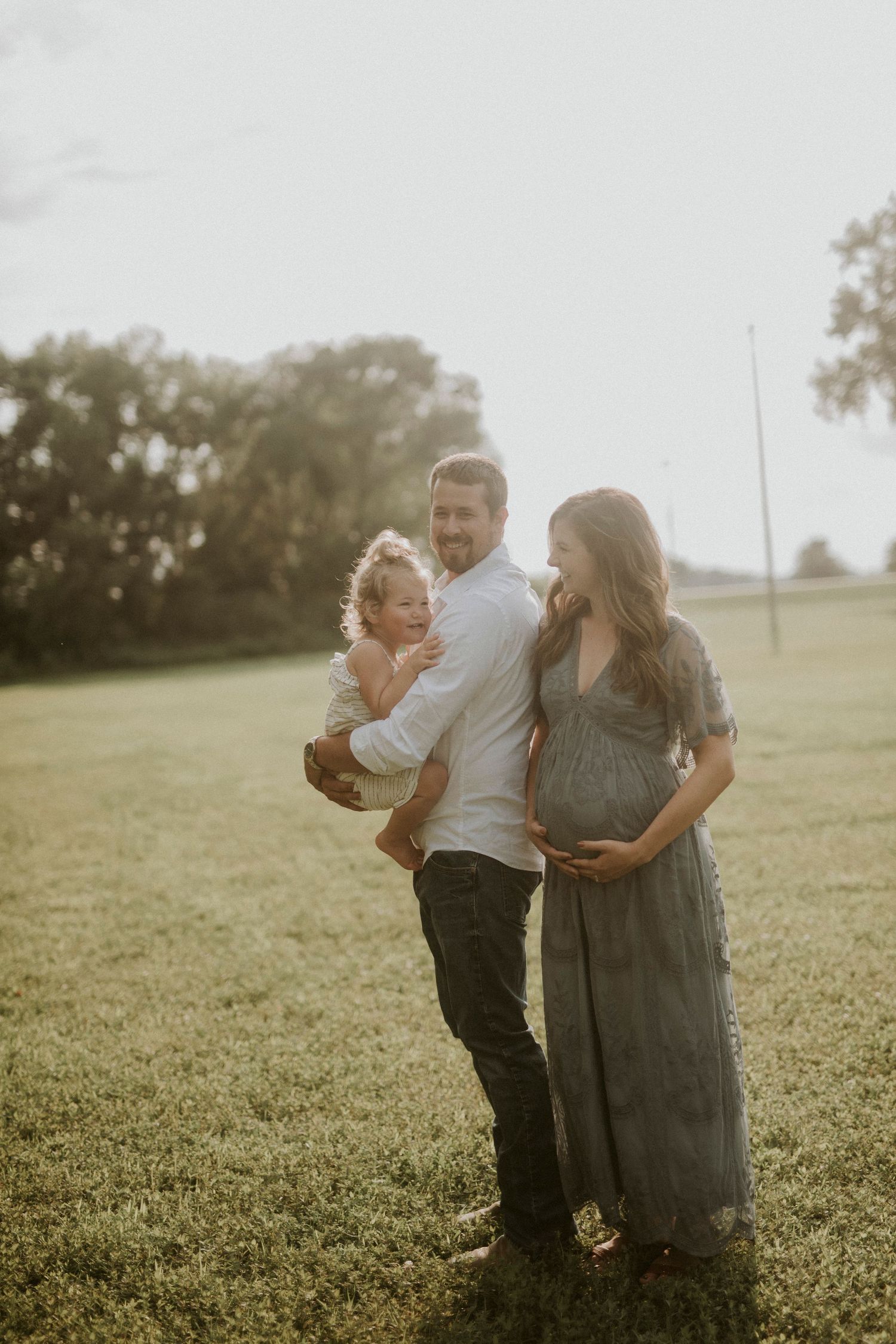 A family shares a tender moment together in a sunlit grassy field during golden hour.