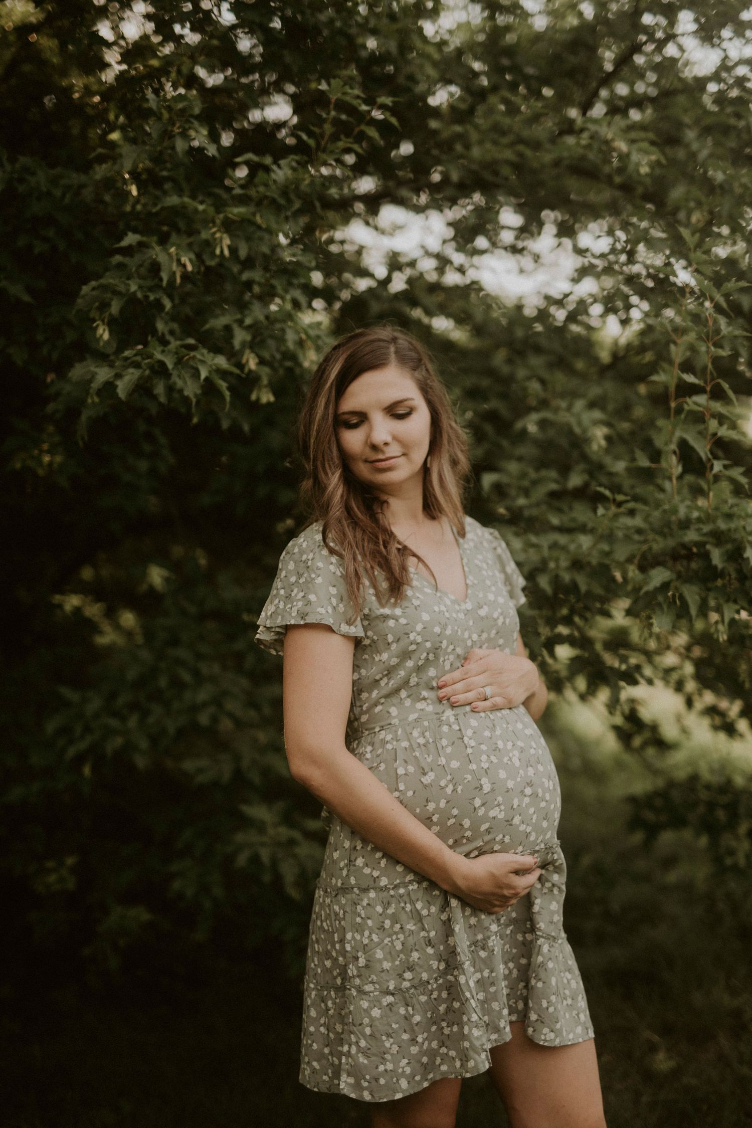 A maternity photoshoot in a natural outdoor setting with green foliage and soft lighting.