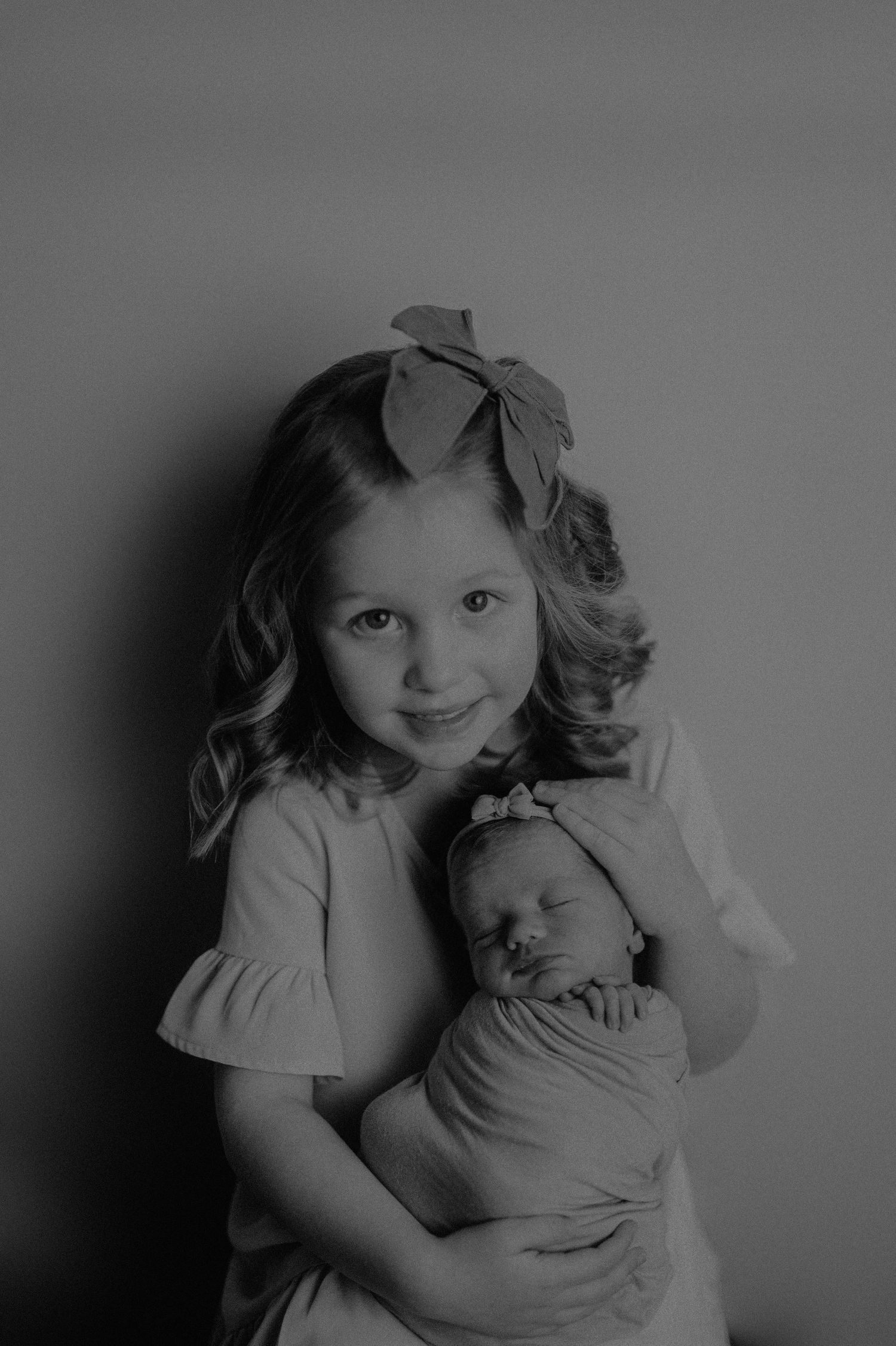 Gentle black and white portraits of siblings with their newborn family member.