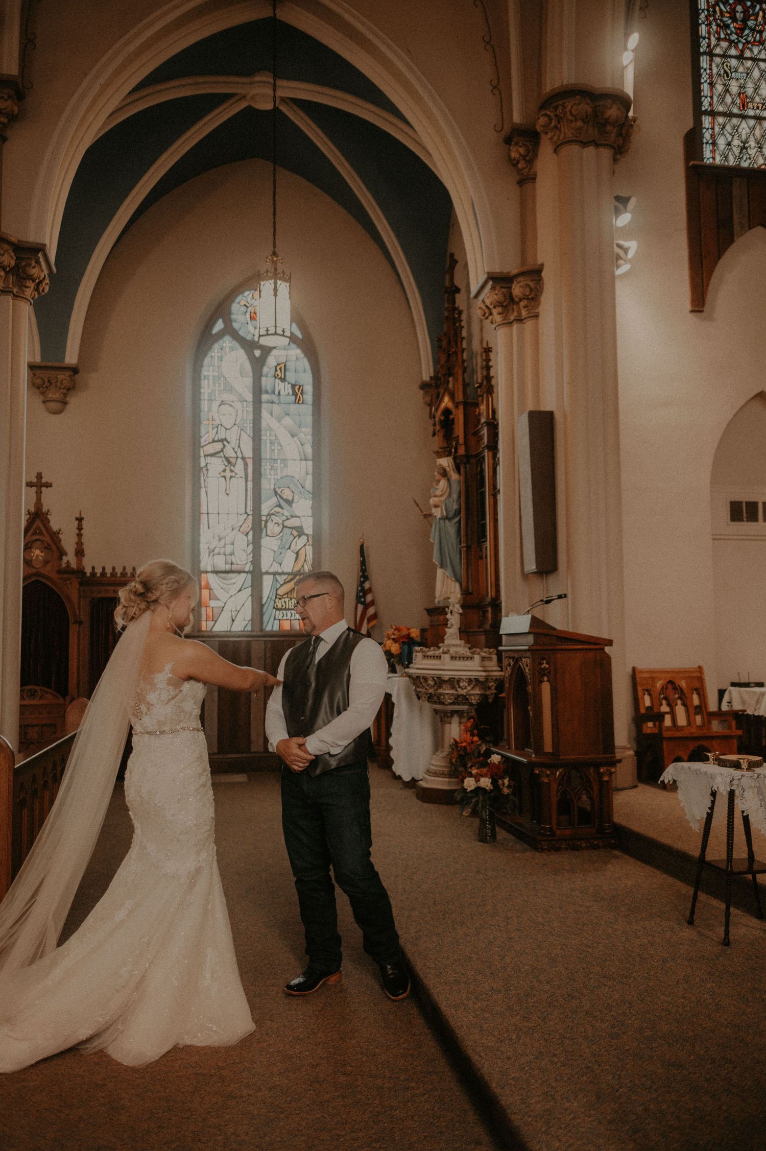 A romantic first look moment unfolds in a beautiful church sanctuary with stained glass windows.