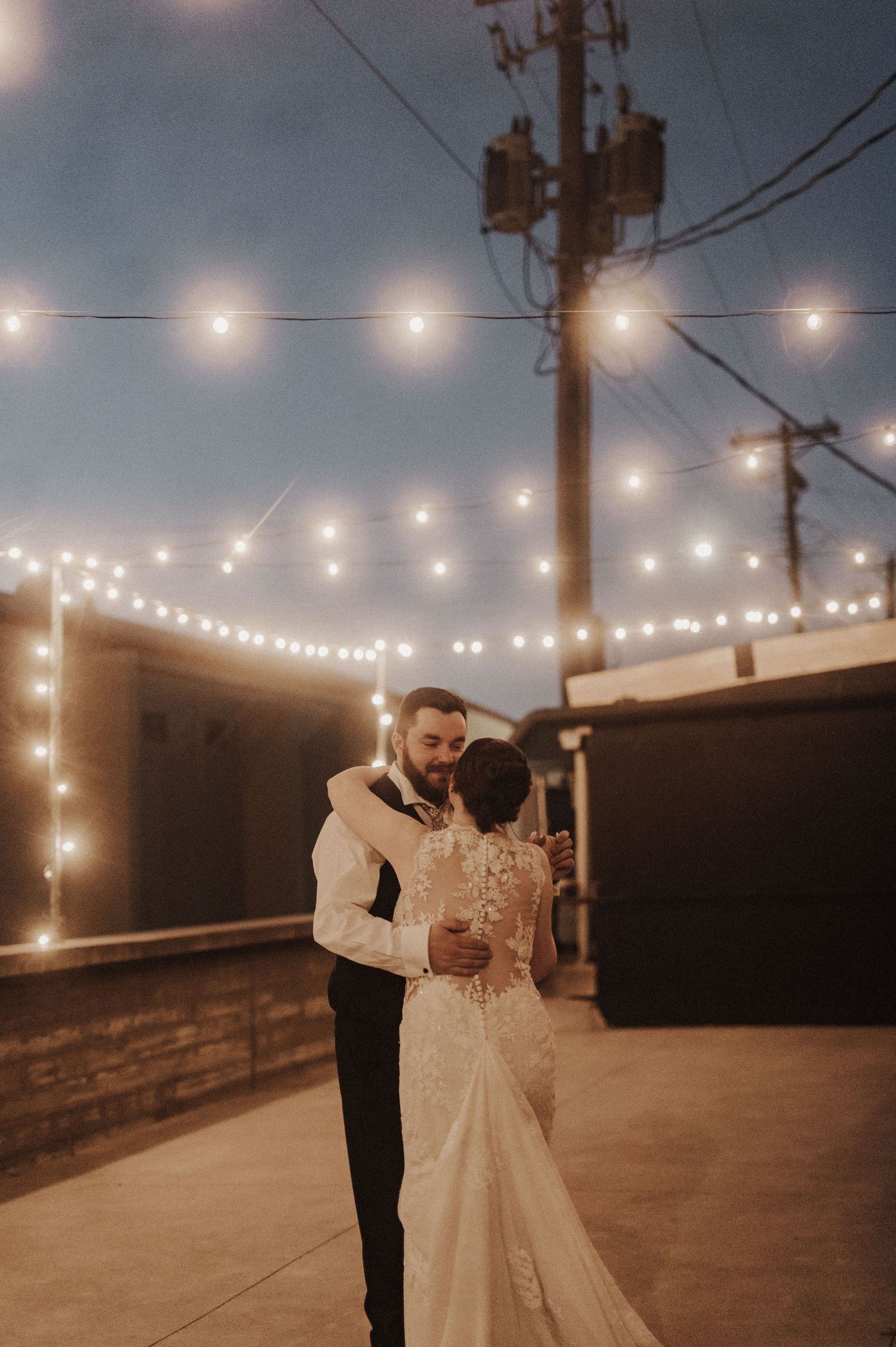 Romantic couple dancing under string lights at dusk on a rooftop.