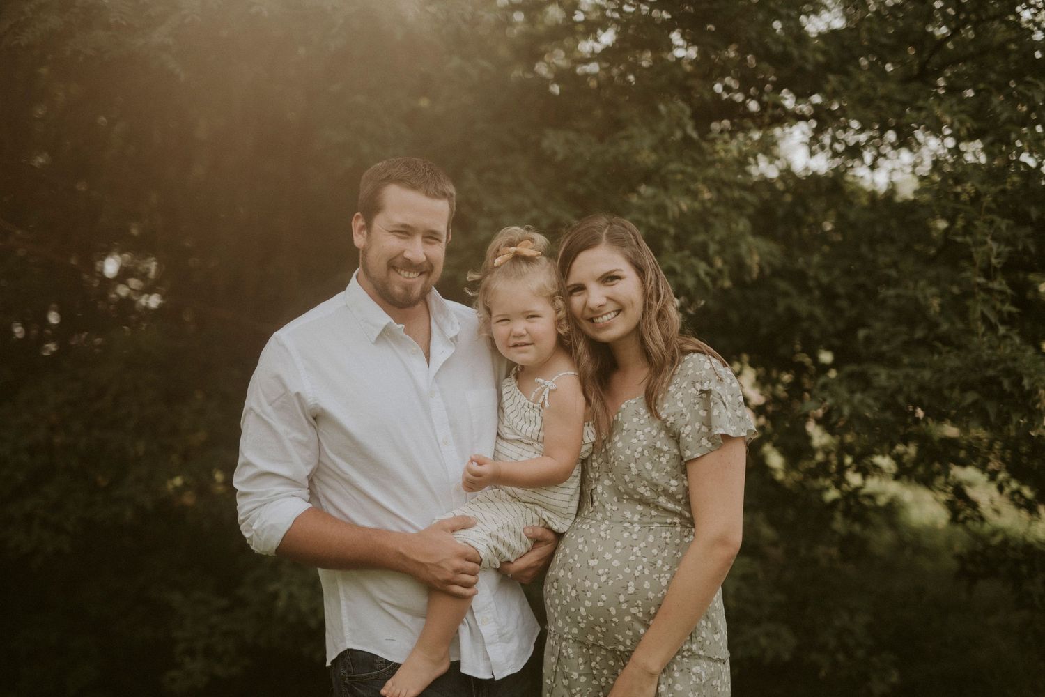 A loving family embraces outdoors during a golden hour photoshoot in a natural setting.