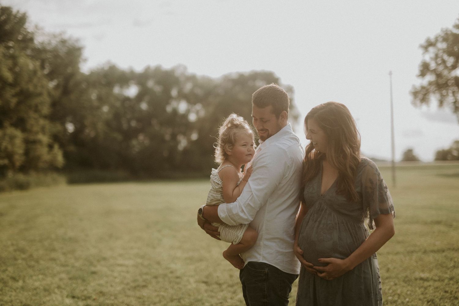 A romantic couple embraces in a sunlit field during a golden hour photoshoot session.