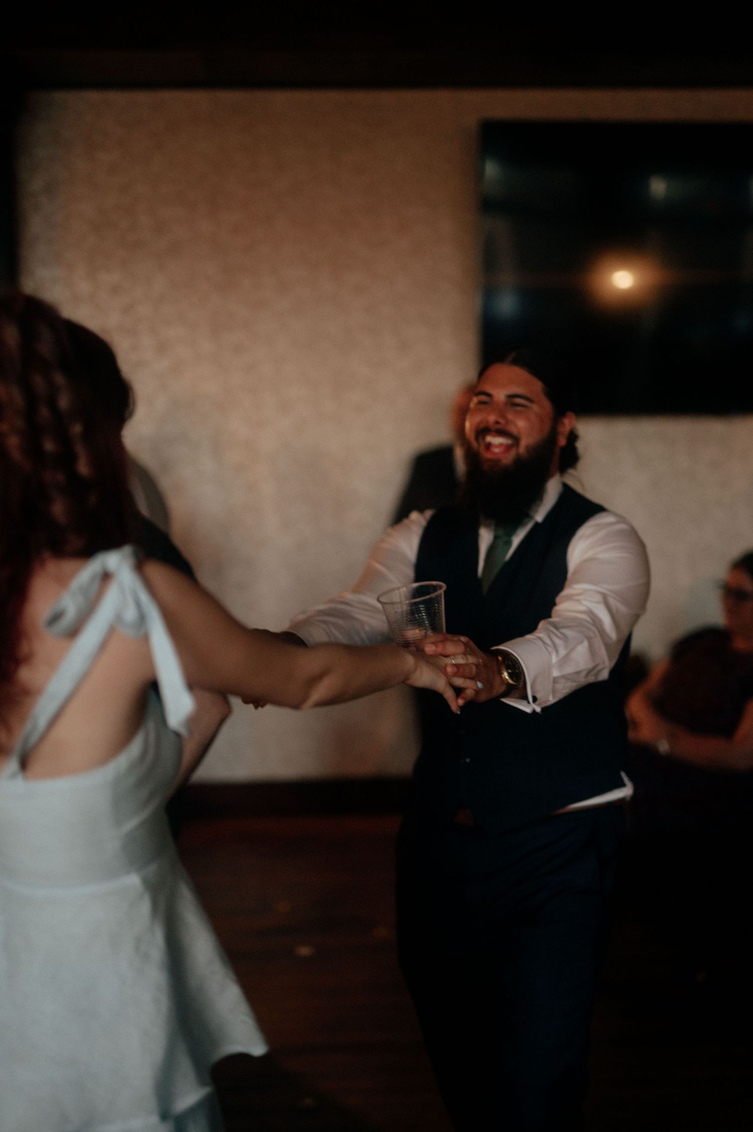 Wedding guests dancing together at an evening reception with warm lighting.