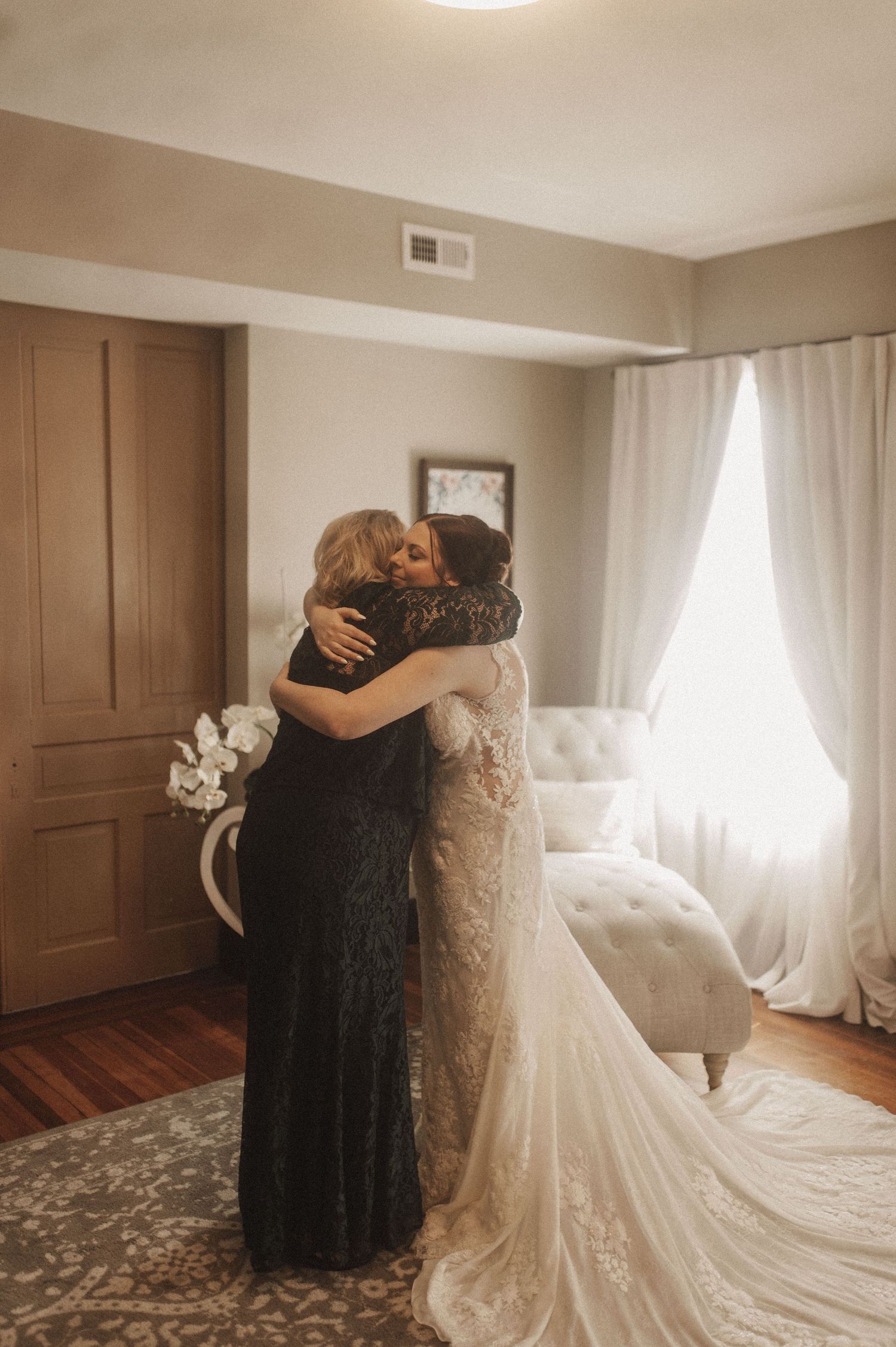 A heartfelt embrace captured in a sunlit room with elegant white curtains and hardwood floors.