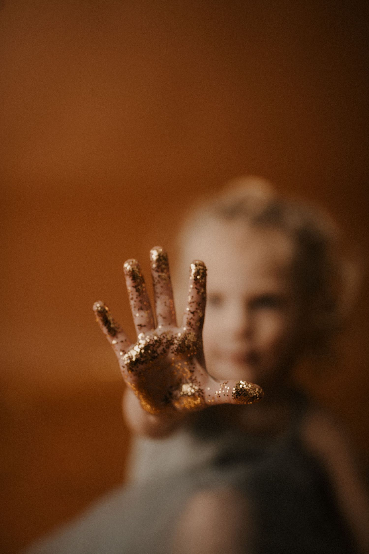 Small hand covered in glitter sparkles against a warm brown background creating a magical effect.