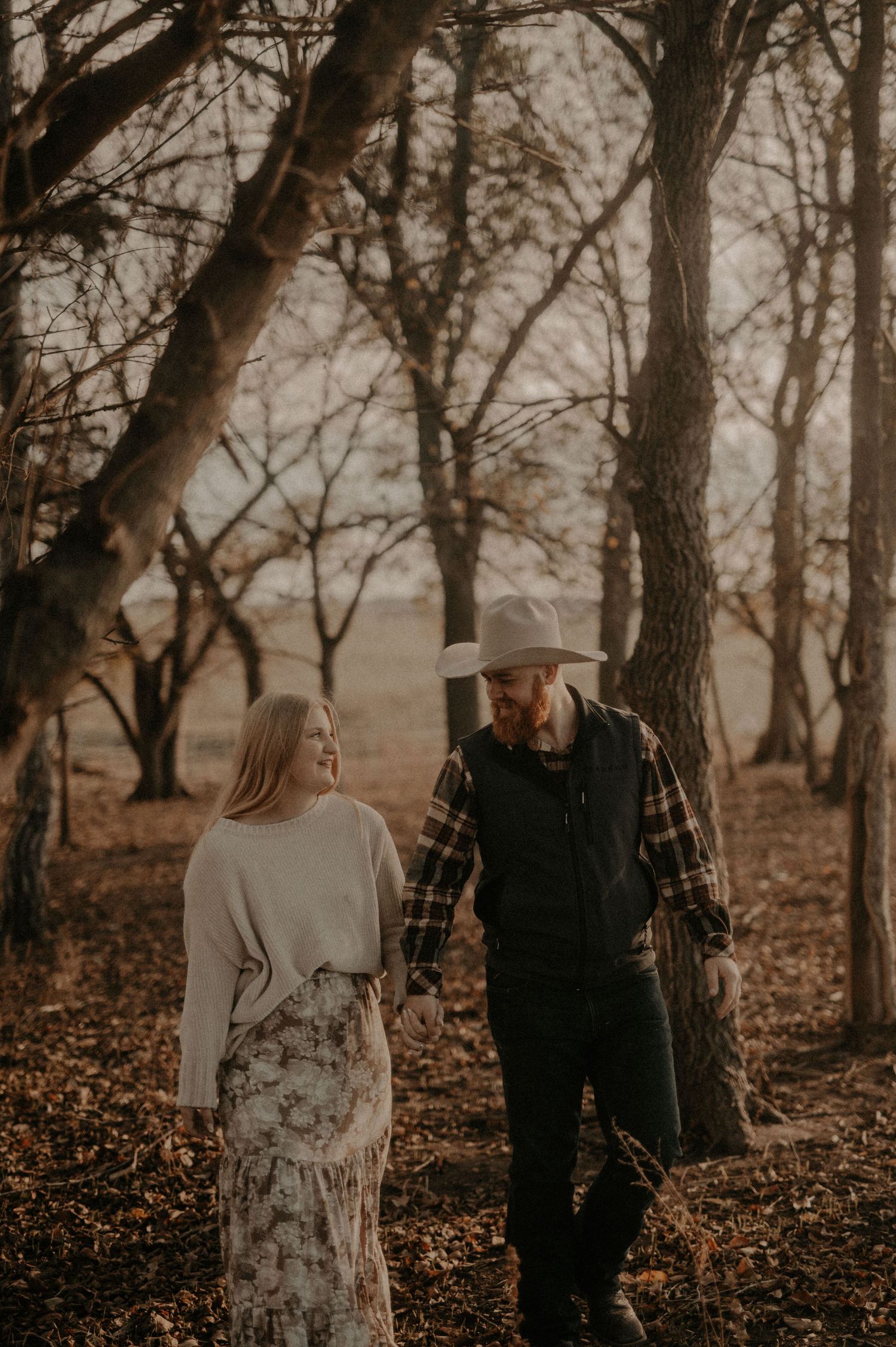 A couple walking through a wooded area with fallen autumn leaves.